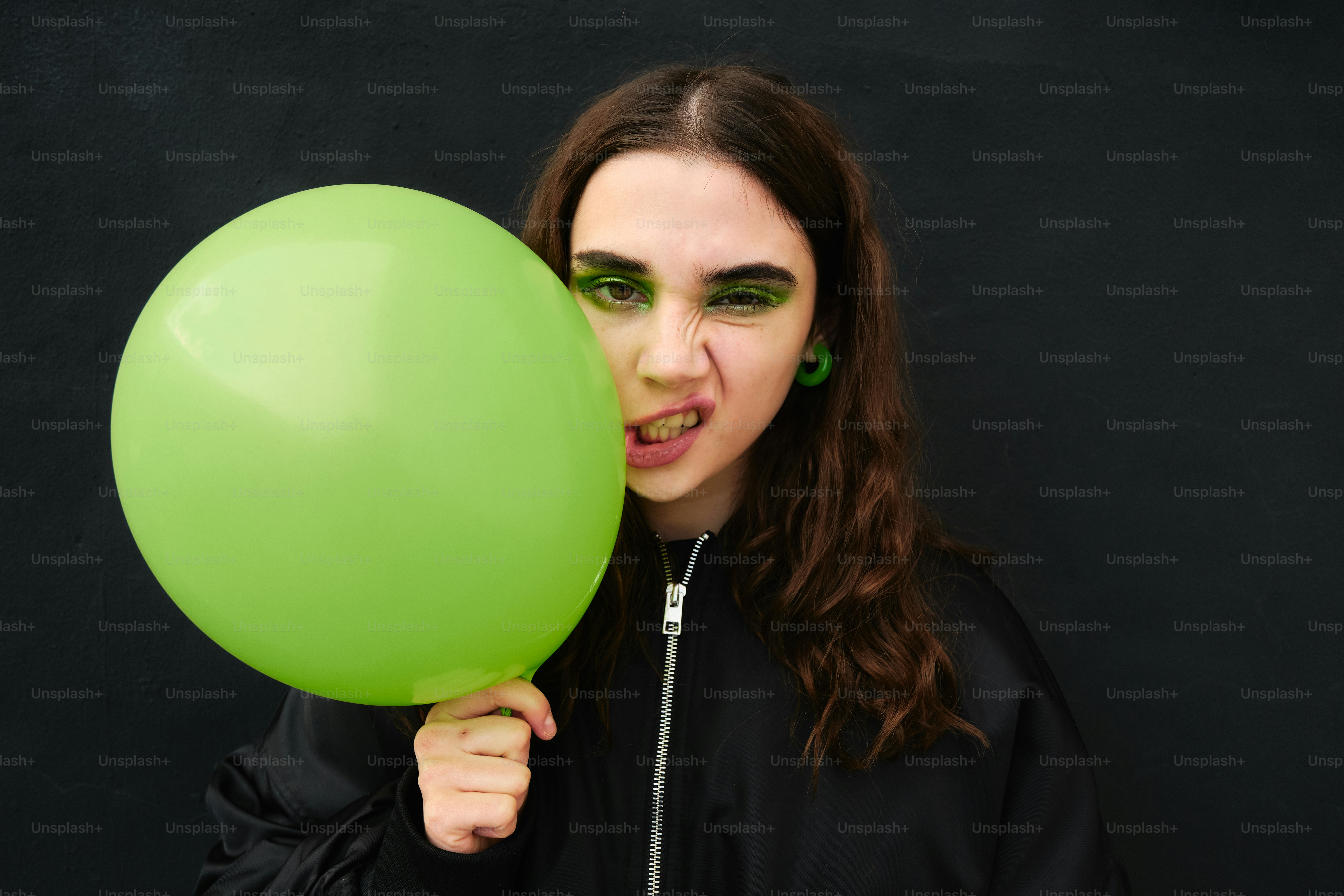 A woman holding a green balloon in front of her face
