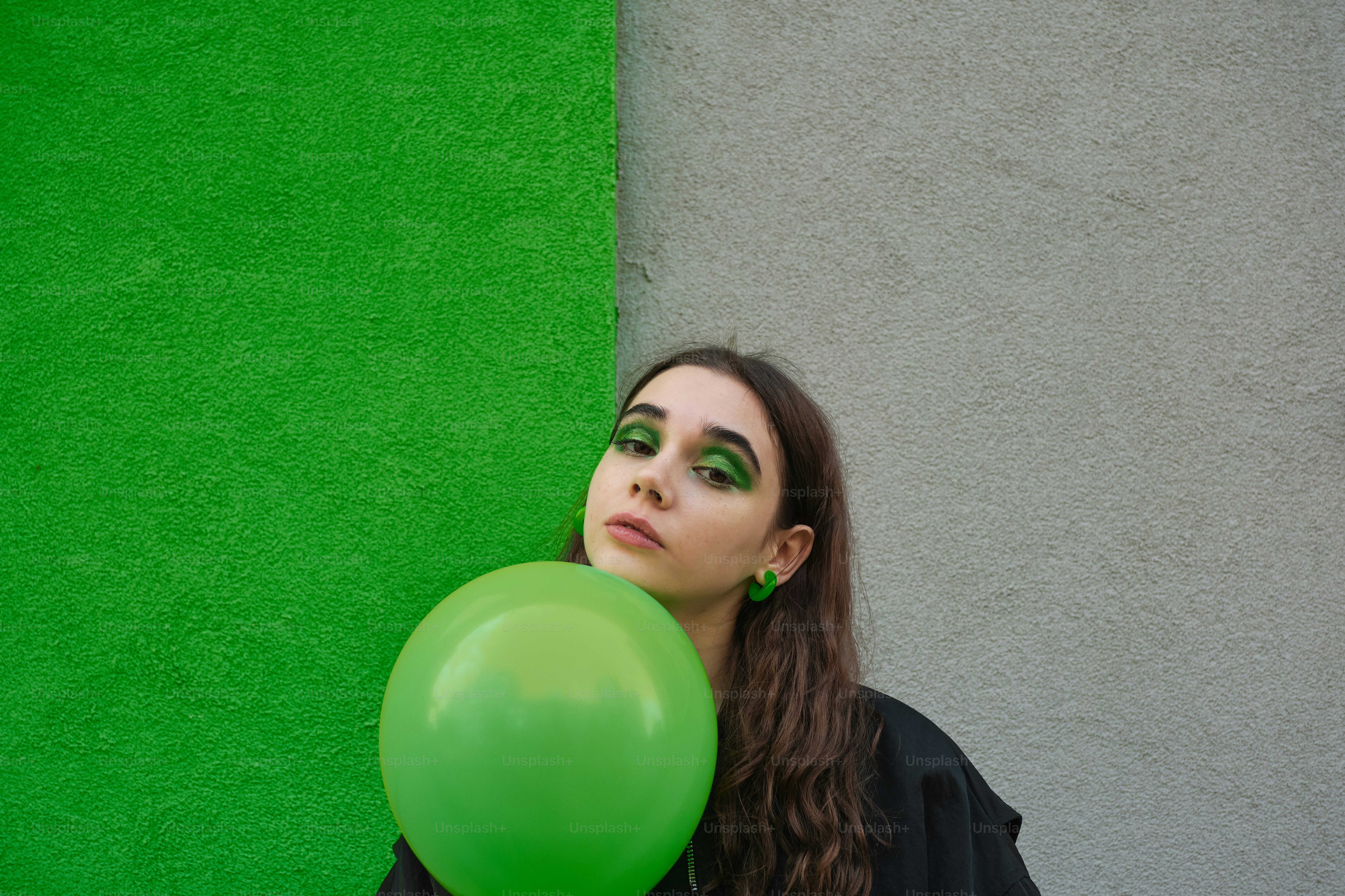 Uma mulher segurando um balão verde na frente de uma parede verde