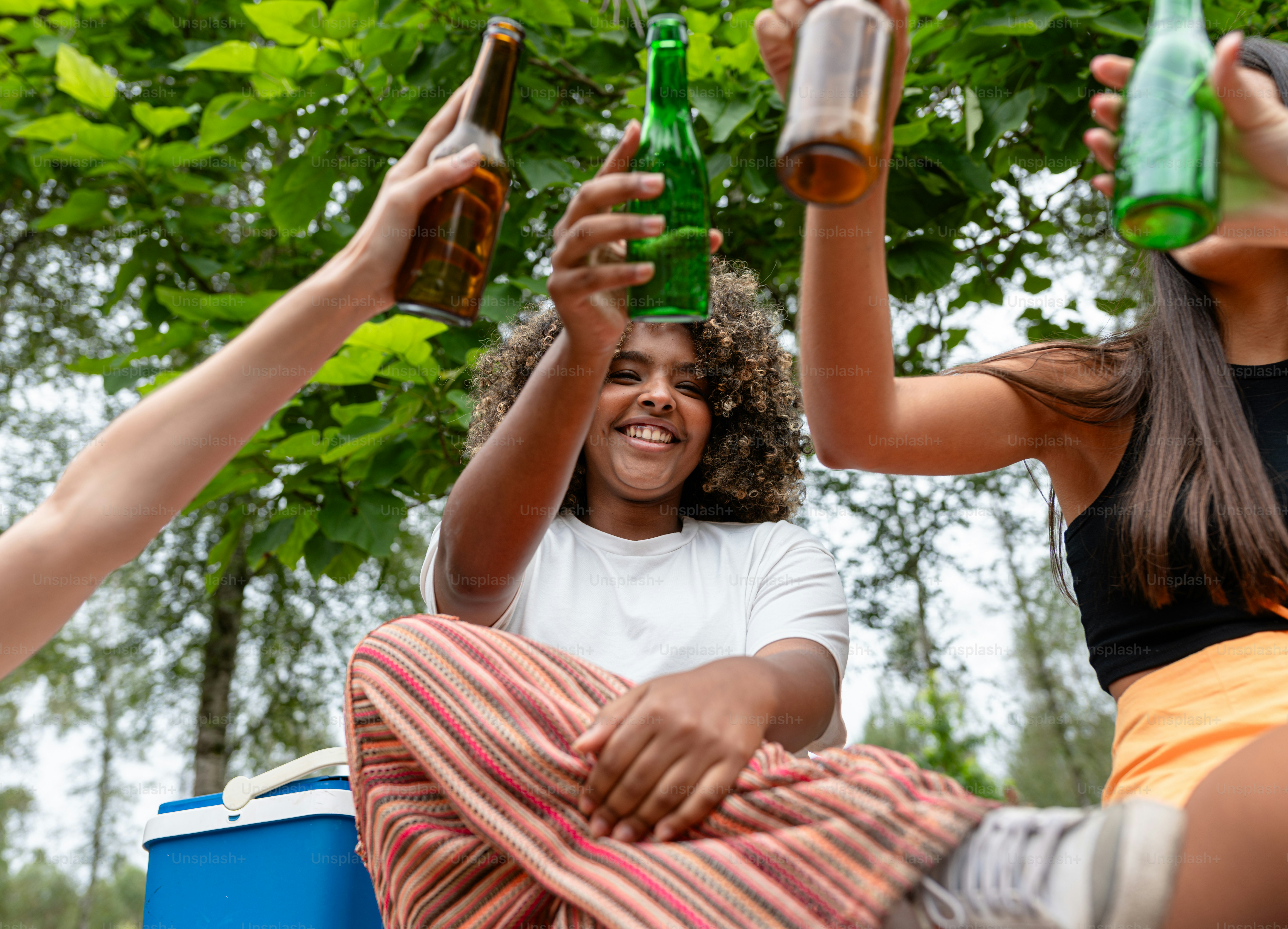 A group of people sitting around each other holding up beer bottles