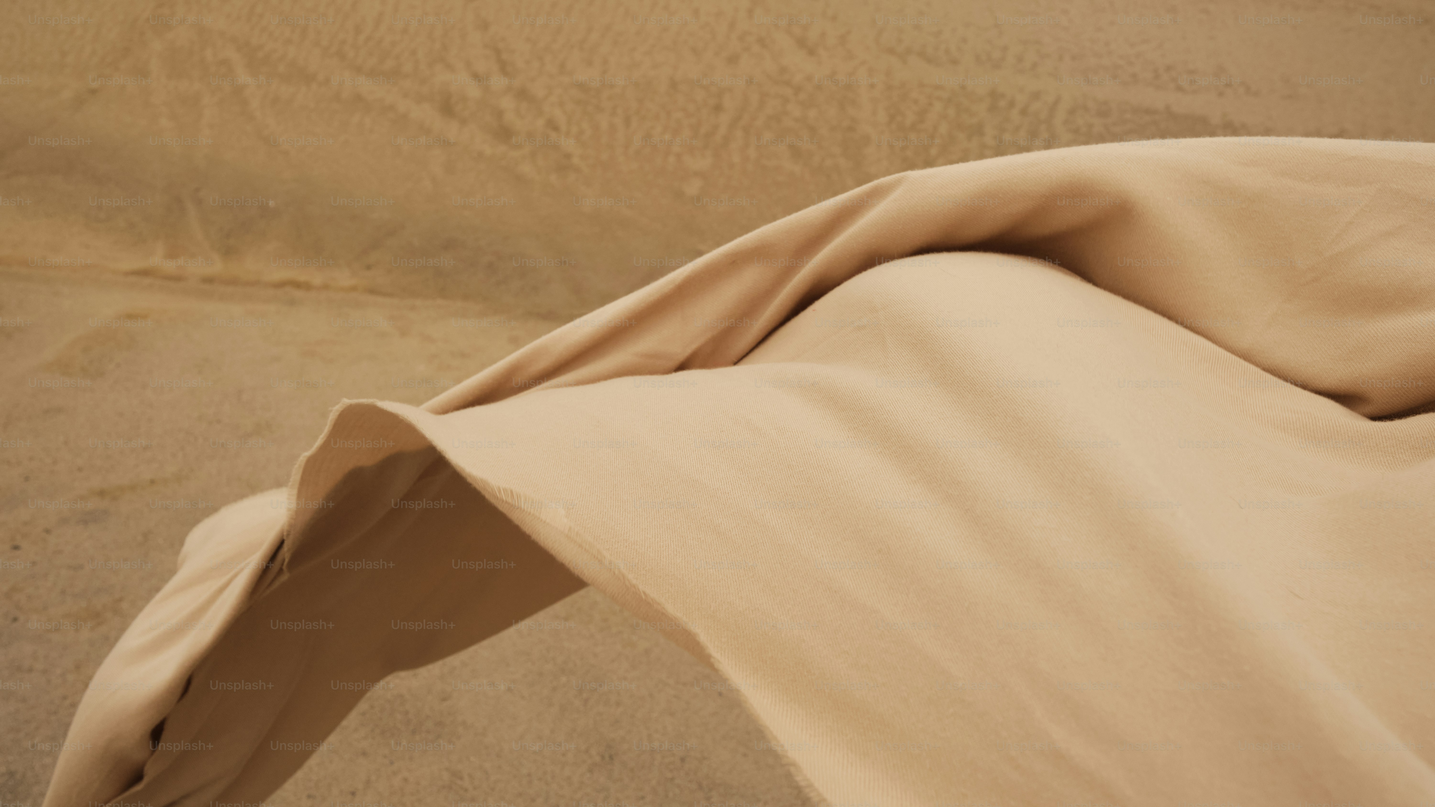 A bed covered in a tan sheet and pillows
