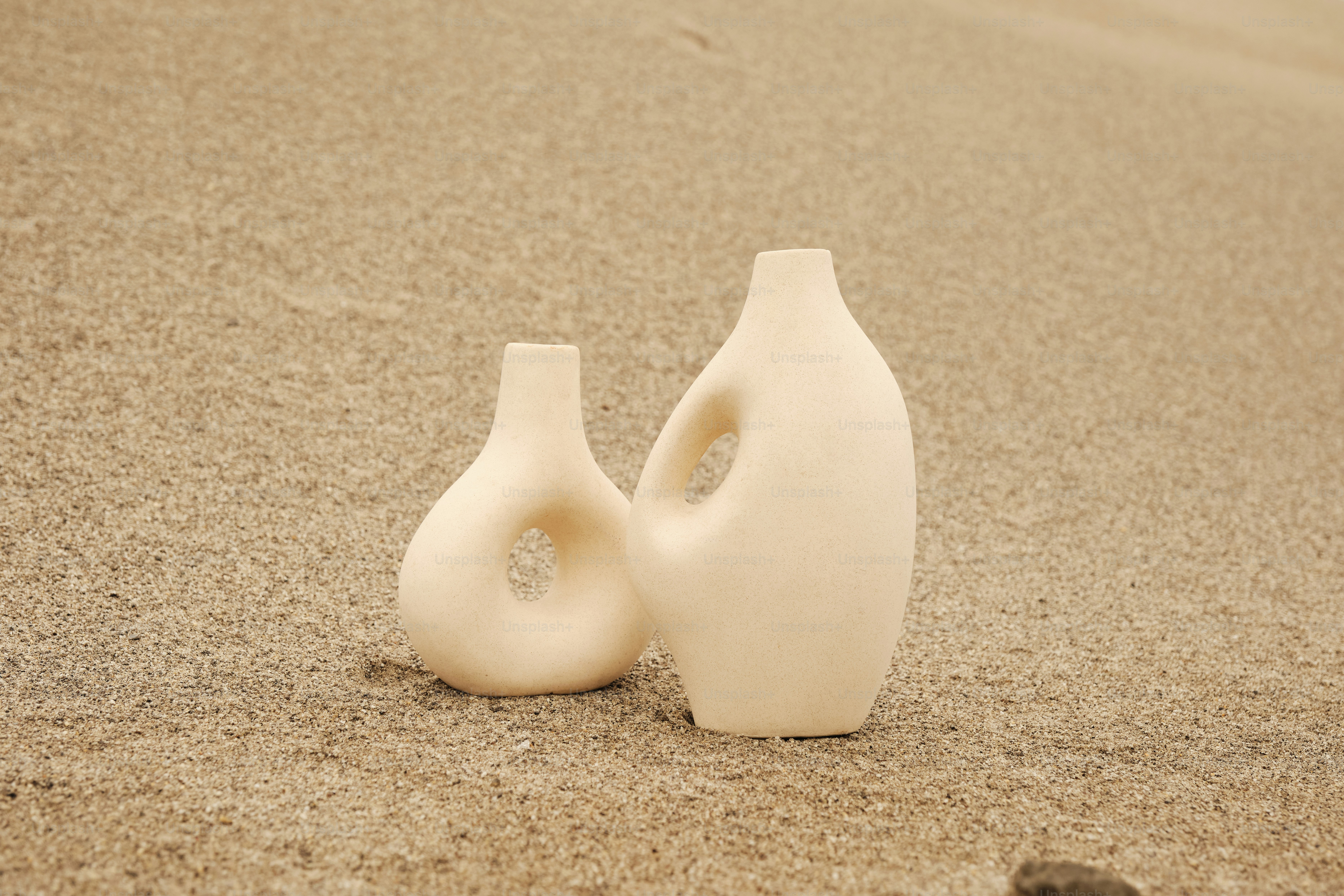 Ein paar weiße Vasen stehen auf einem Sandstrand