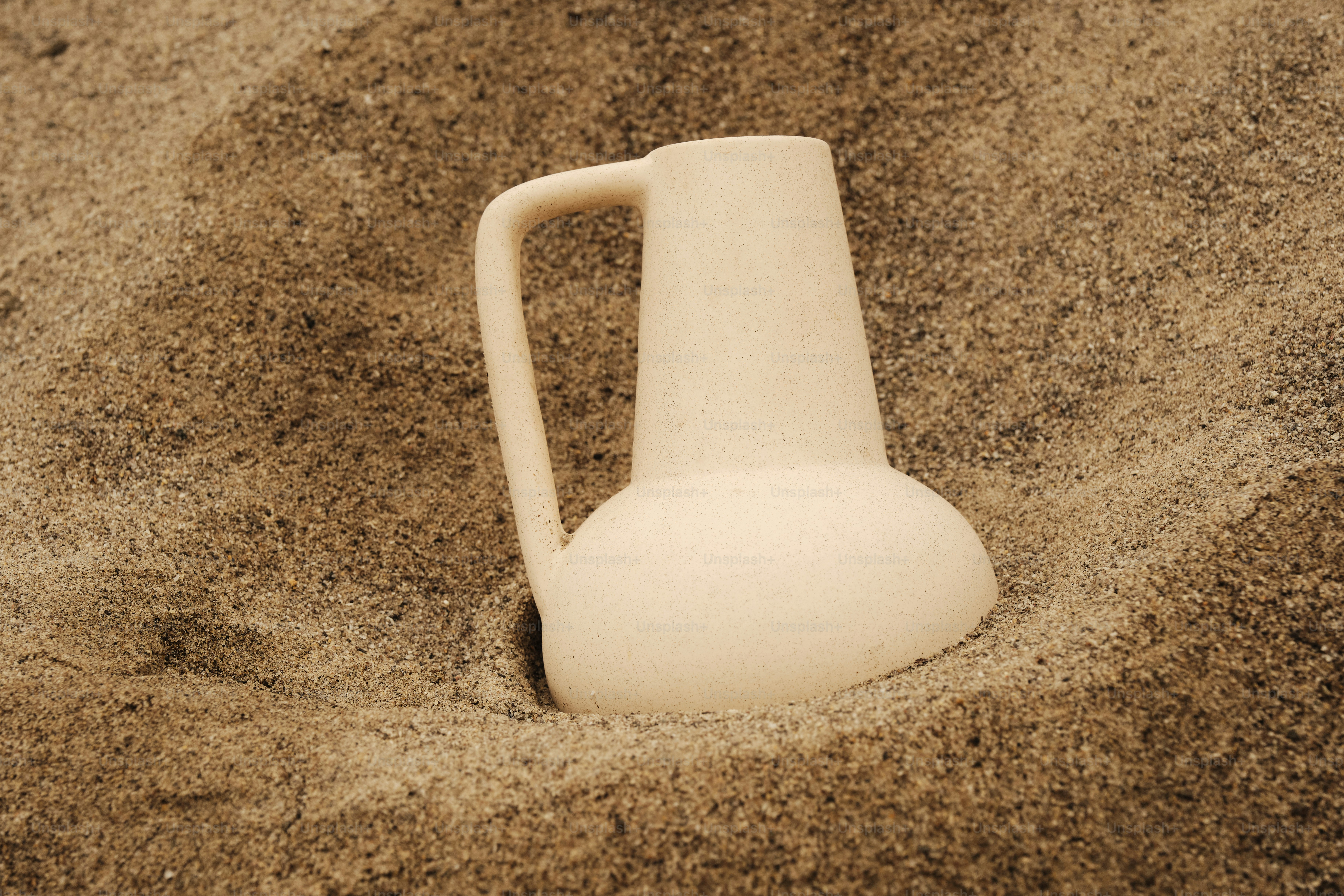 A white pitcher sitting in the sand on the beach