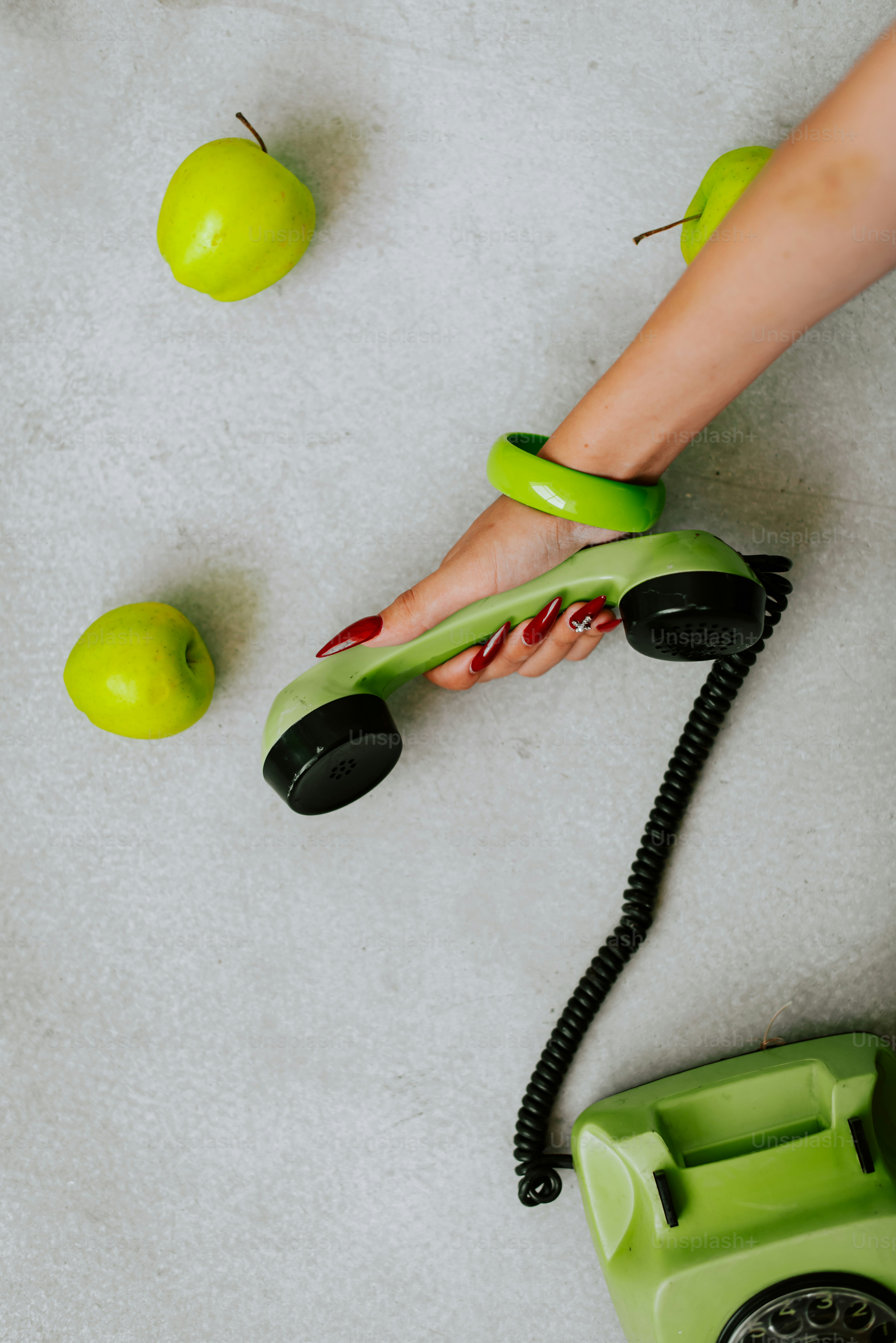 Eine Person hält ein grünes Telefon neben grünen Äpfeln