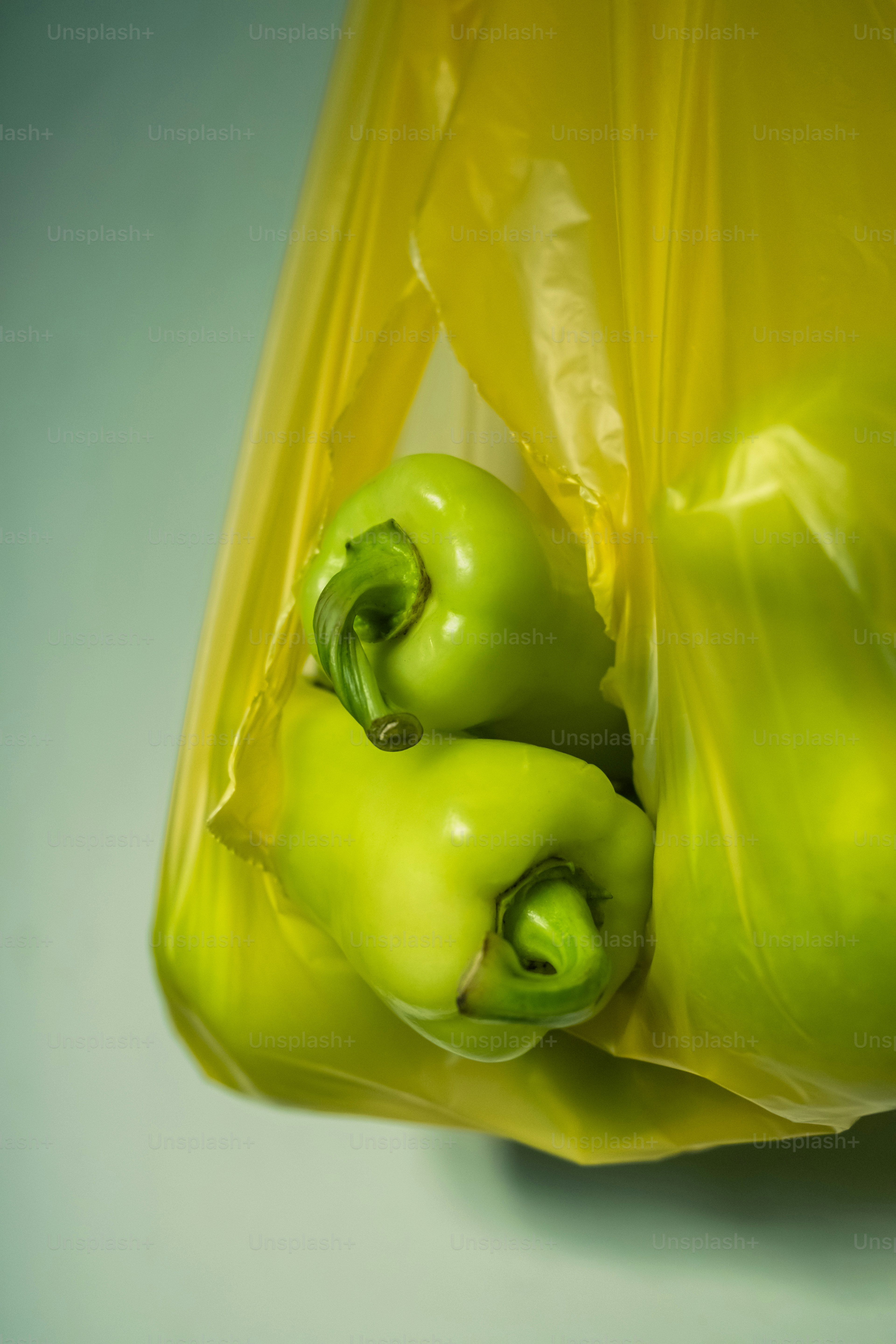 A yellow bag filled with green peppers on top of a table