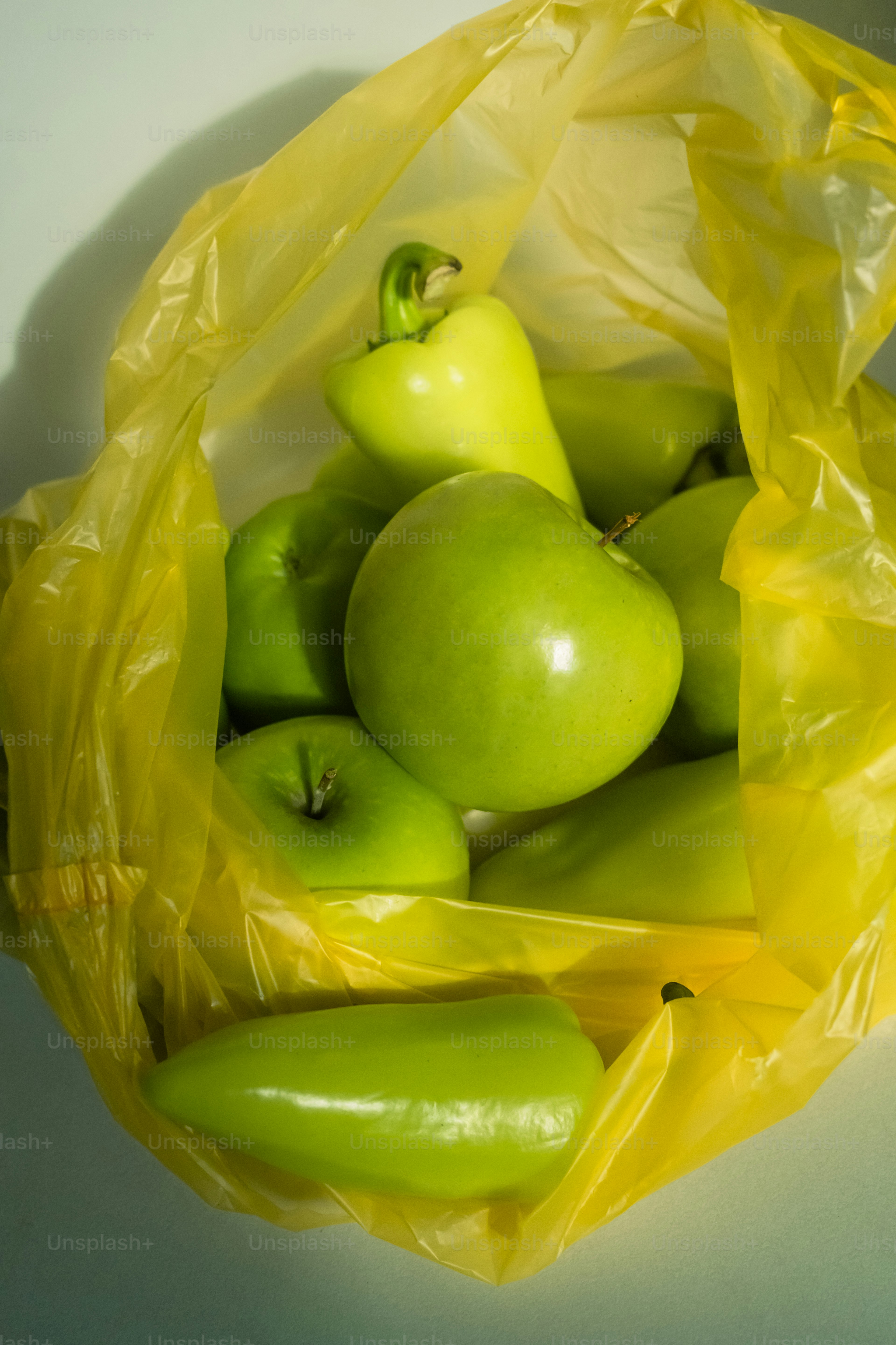 A yellow bag filled with green apples and peppers