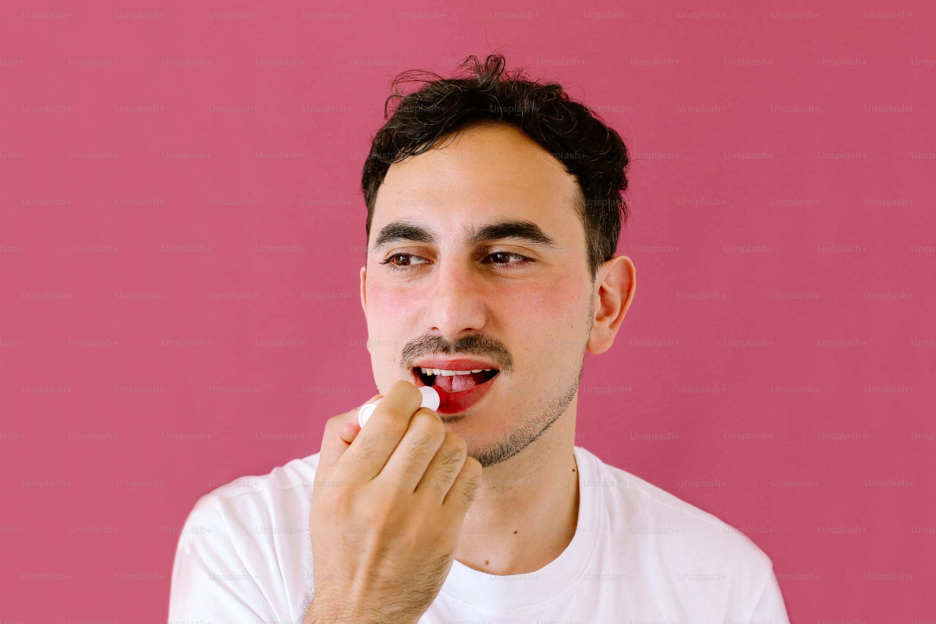 A man is brushing his teeth in front of a pink wall