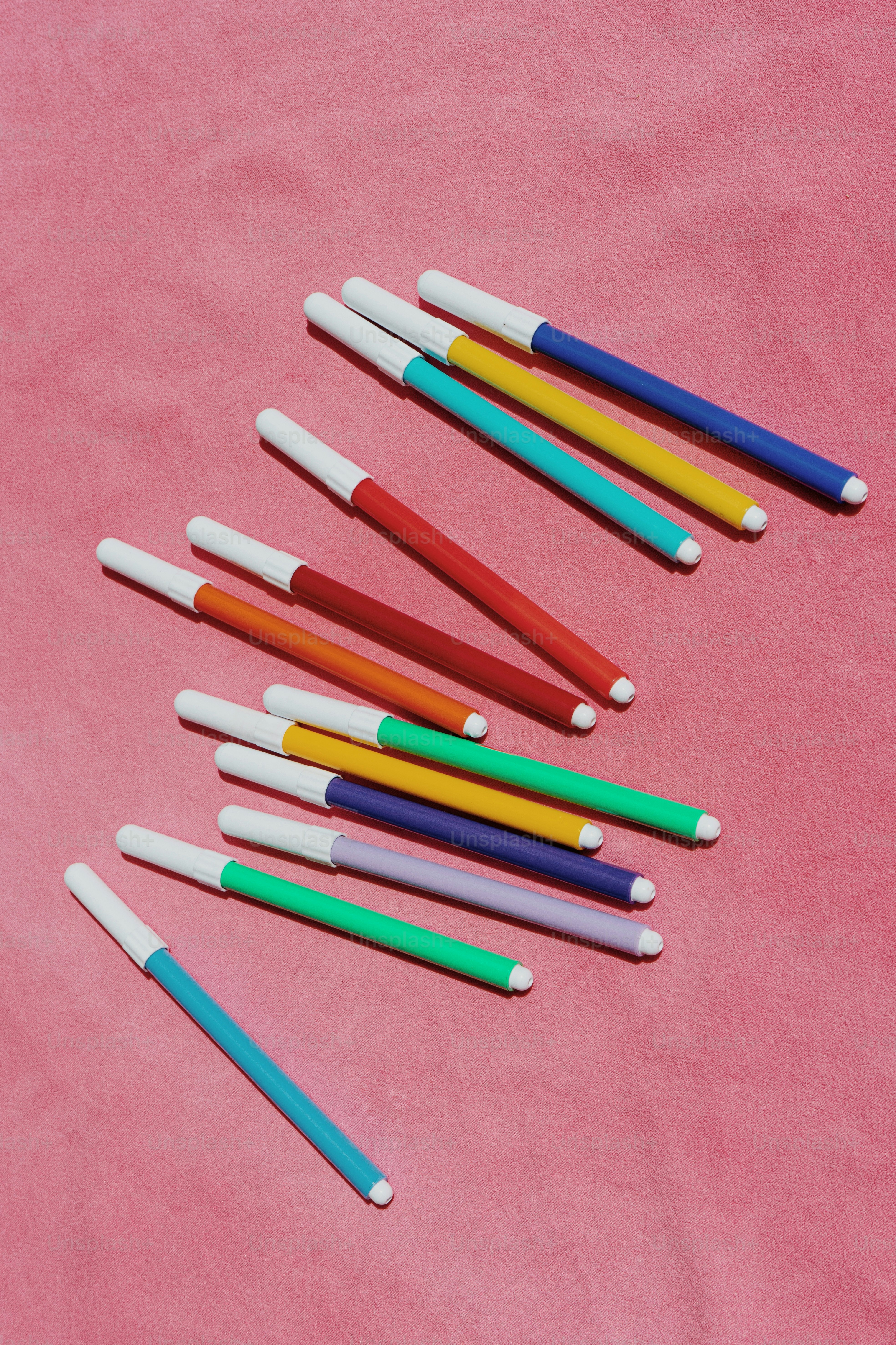 A group of colored pencils laying on a pink surface