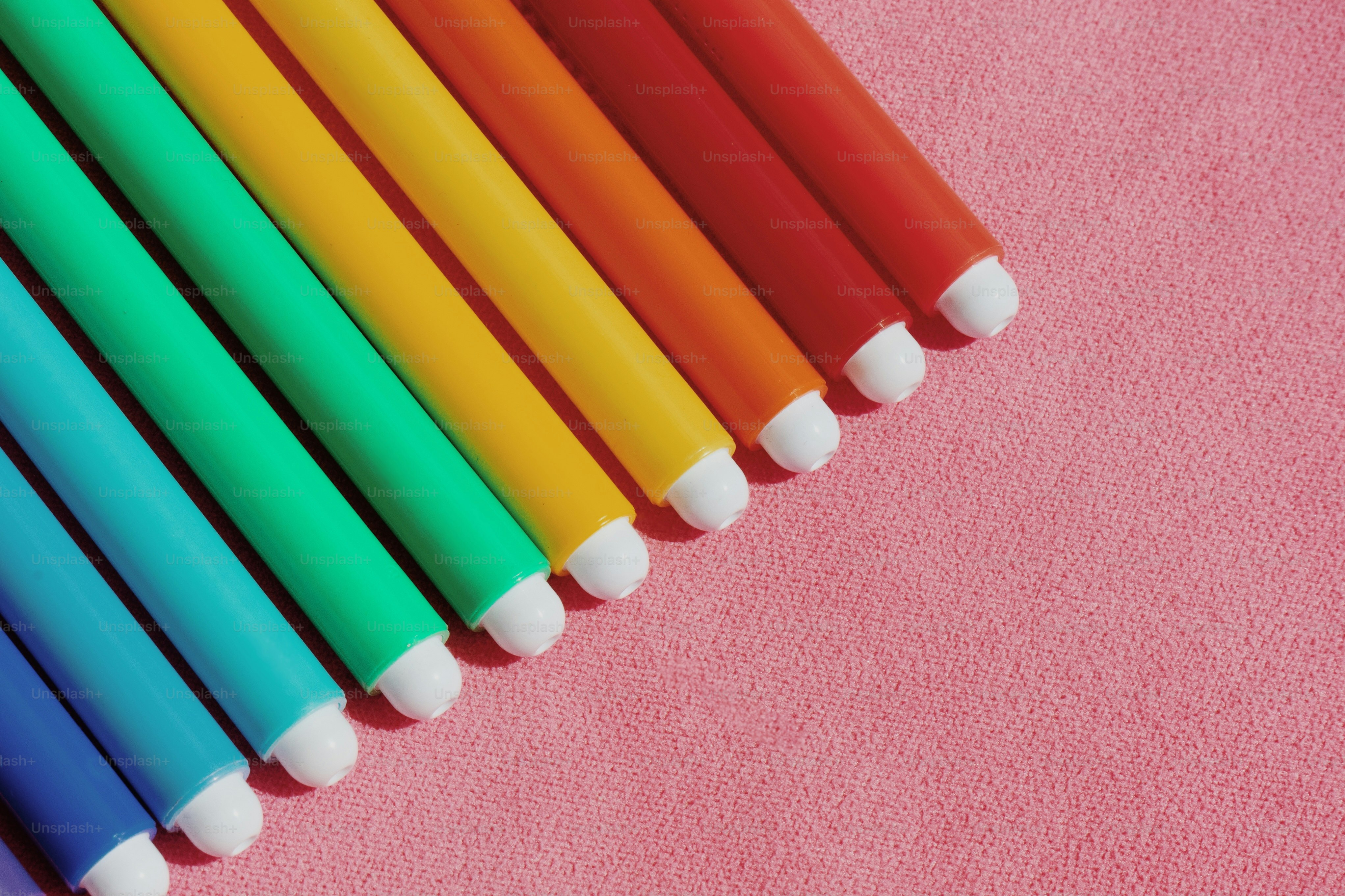 A row of colored pencils on a pink surface
