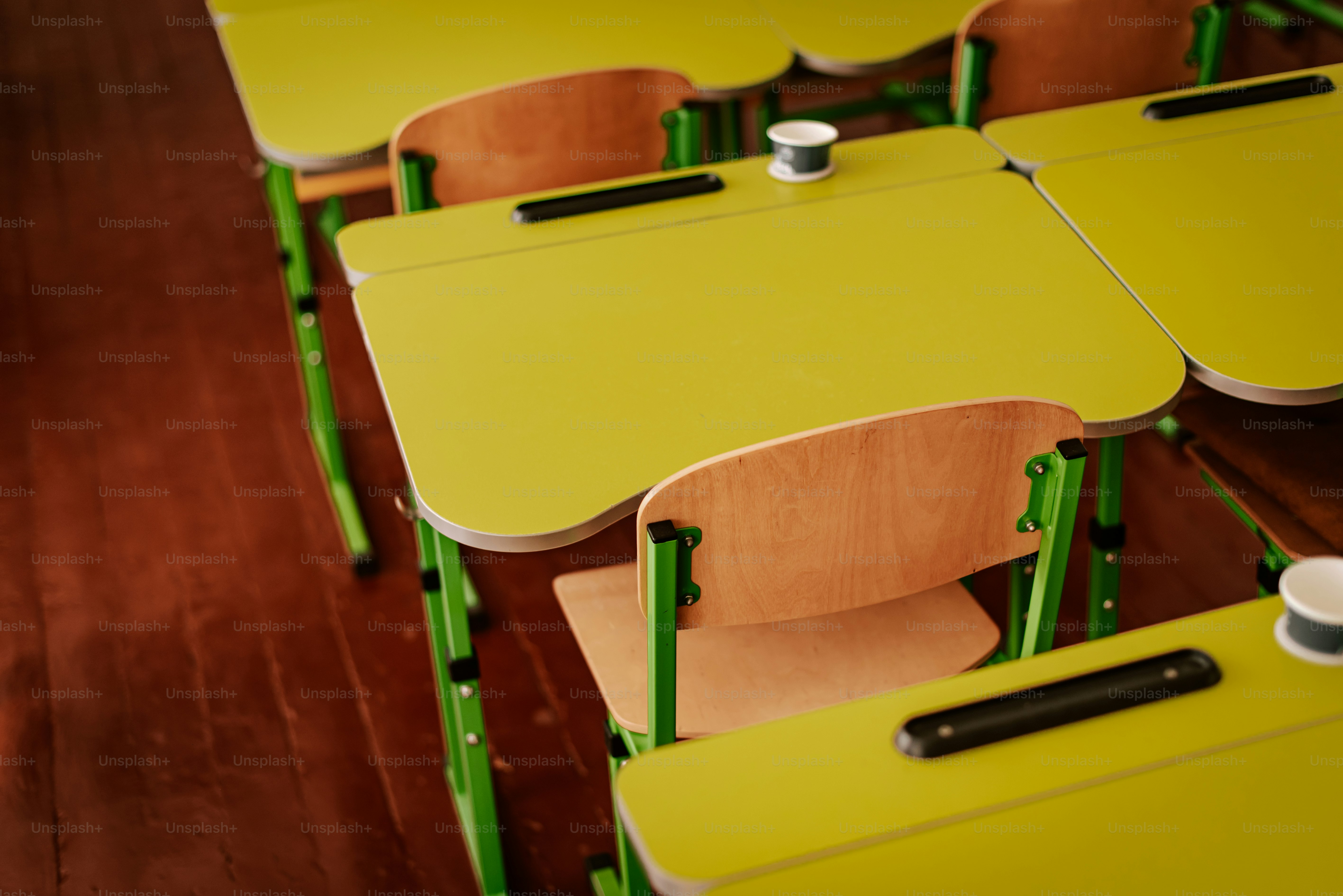 Uma sala de aula cheia de mesas amarelas e cadeiras verdes