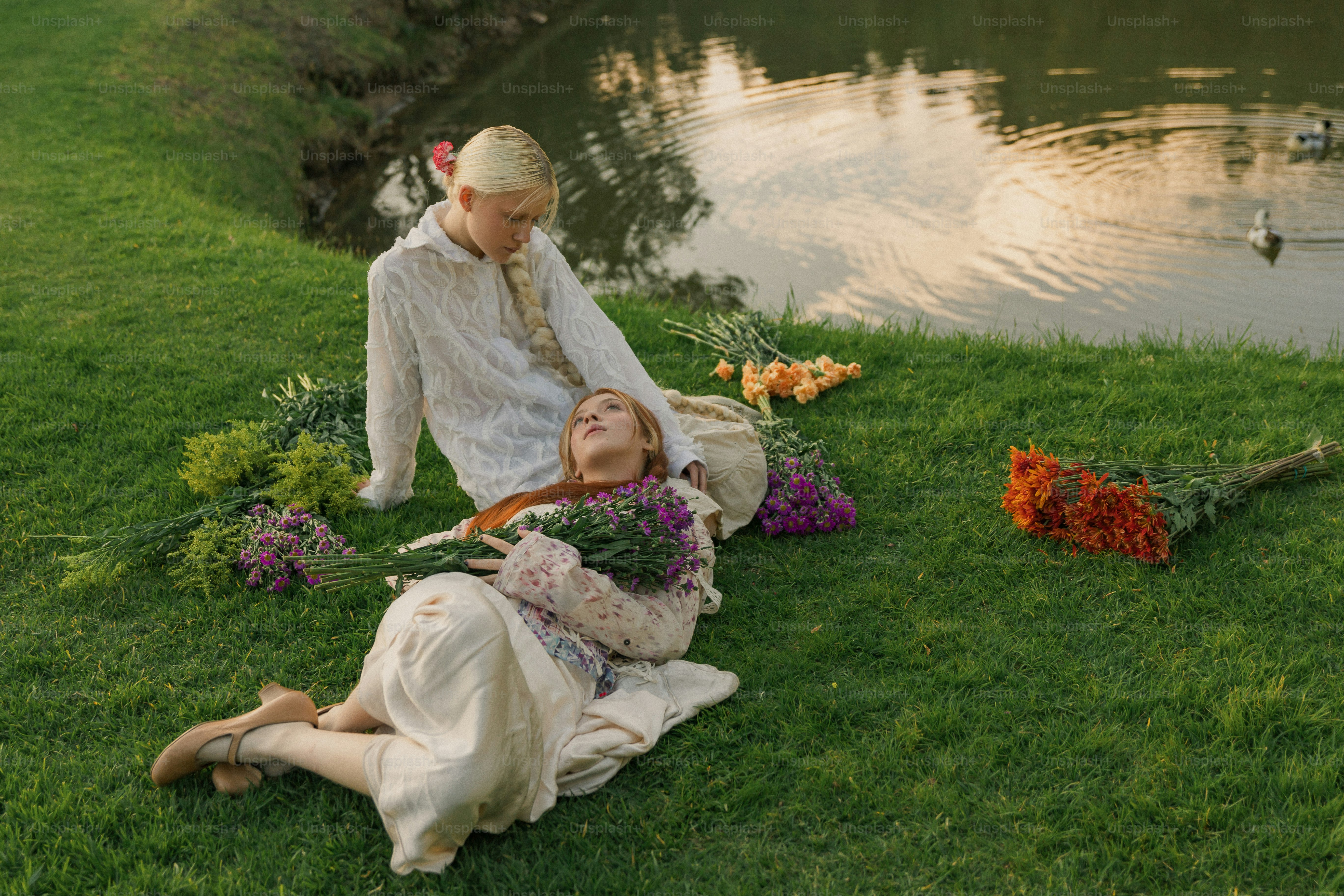 A man and a woman sitting on the grass near a lake photo – Relaxing ...