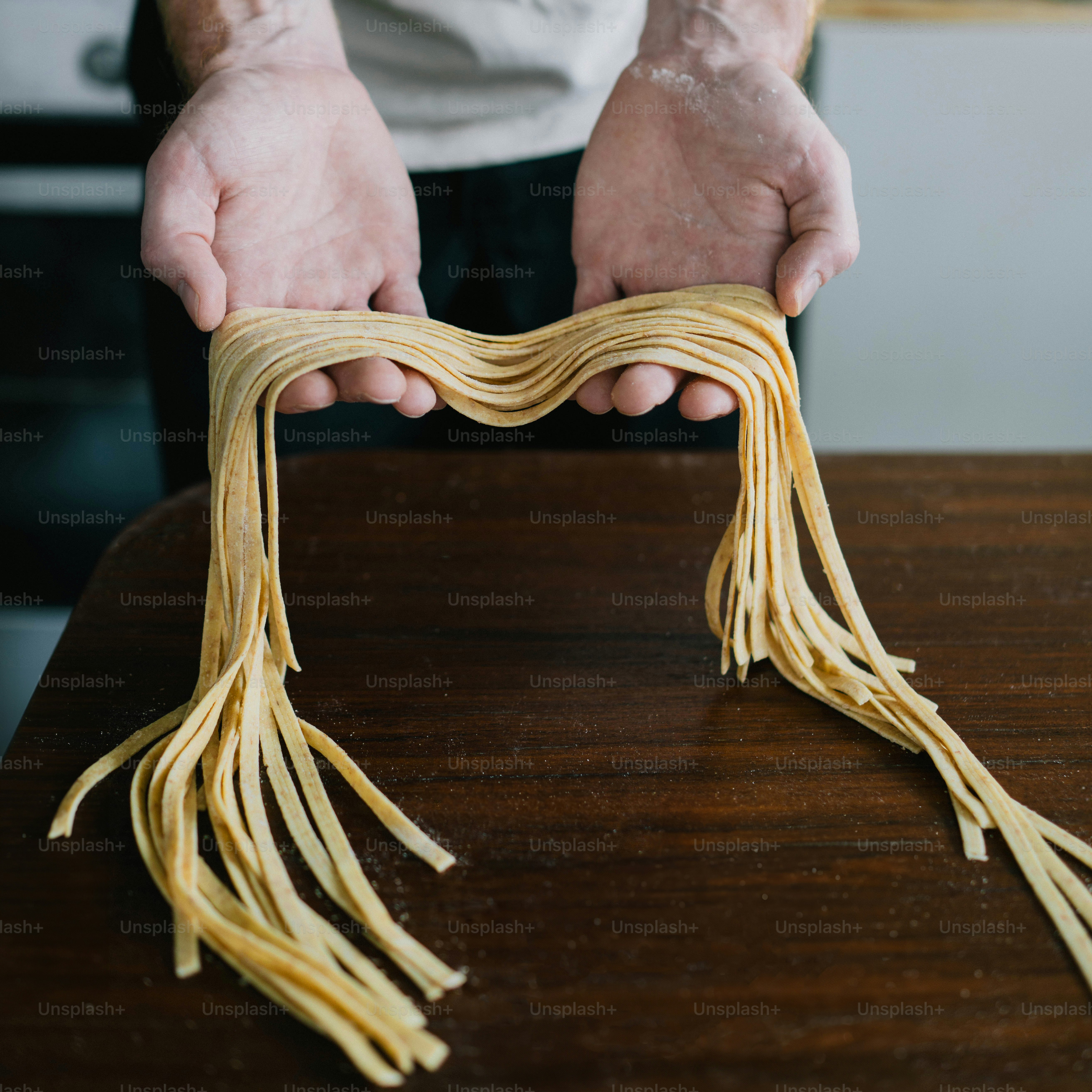 Uma pessoa segurando um monte de macarrão em cima de uma mesa de madeira