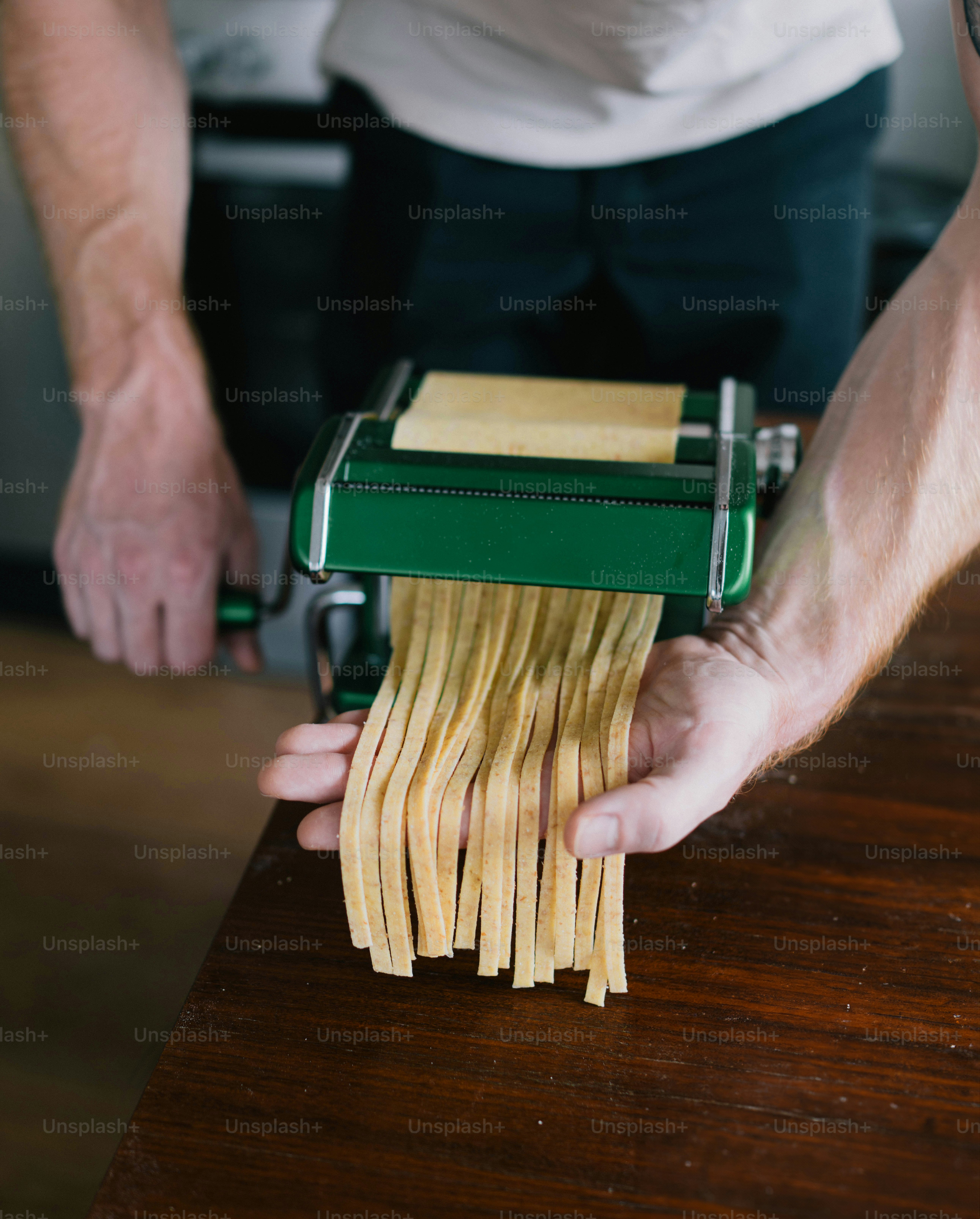 Uma pessoa segurando um cortador de macarrão sobre uma pilha de macarrão