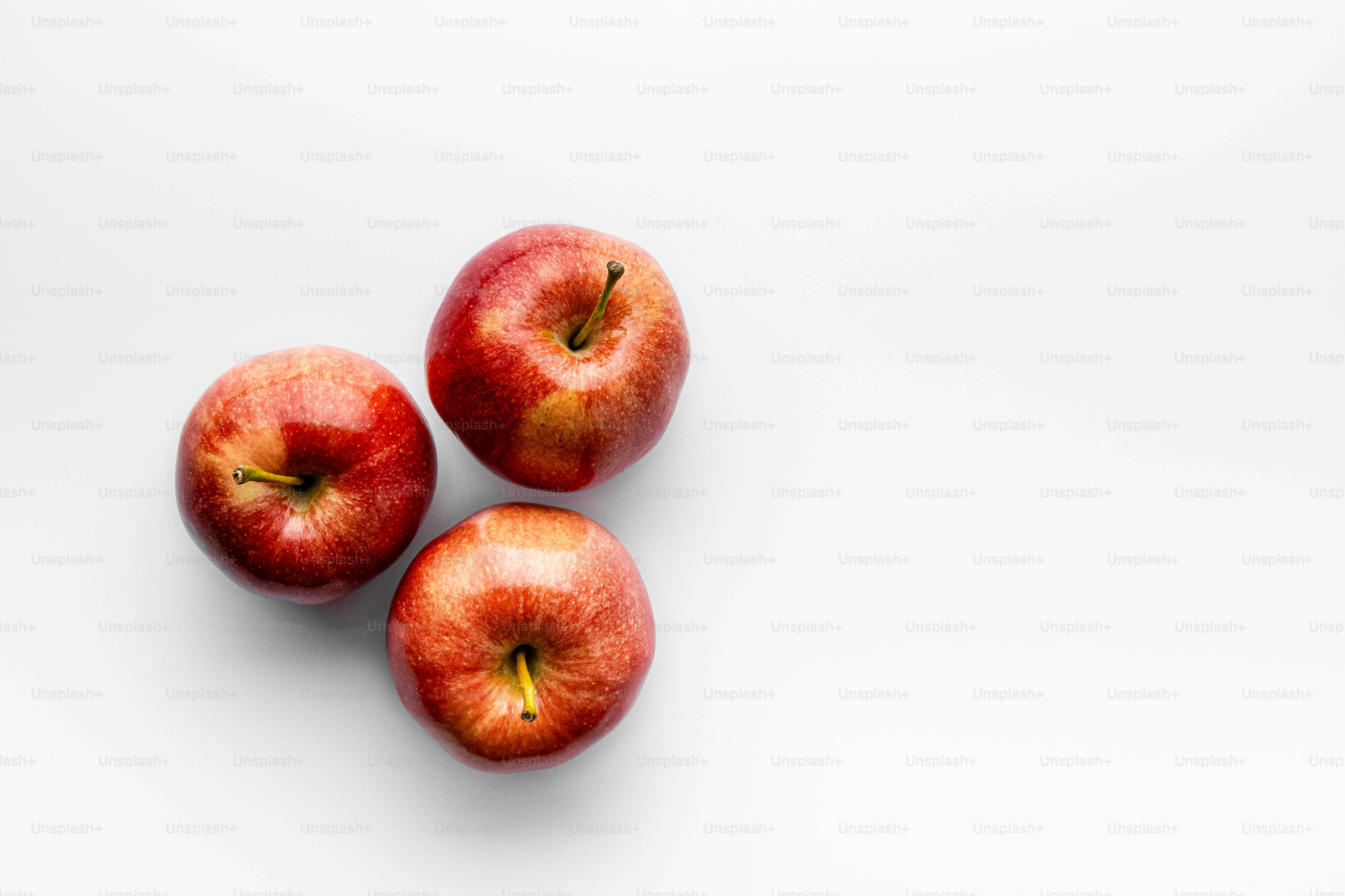 Three apples sitting on top of a white surface
