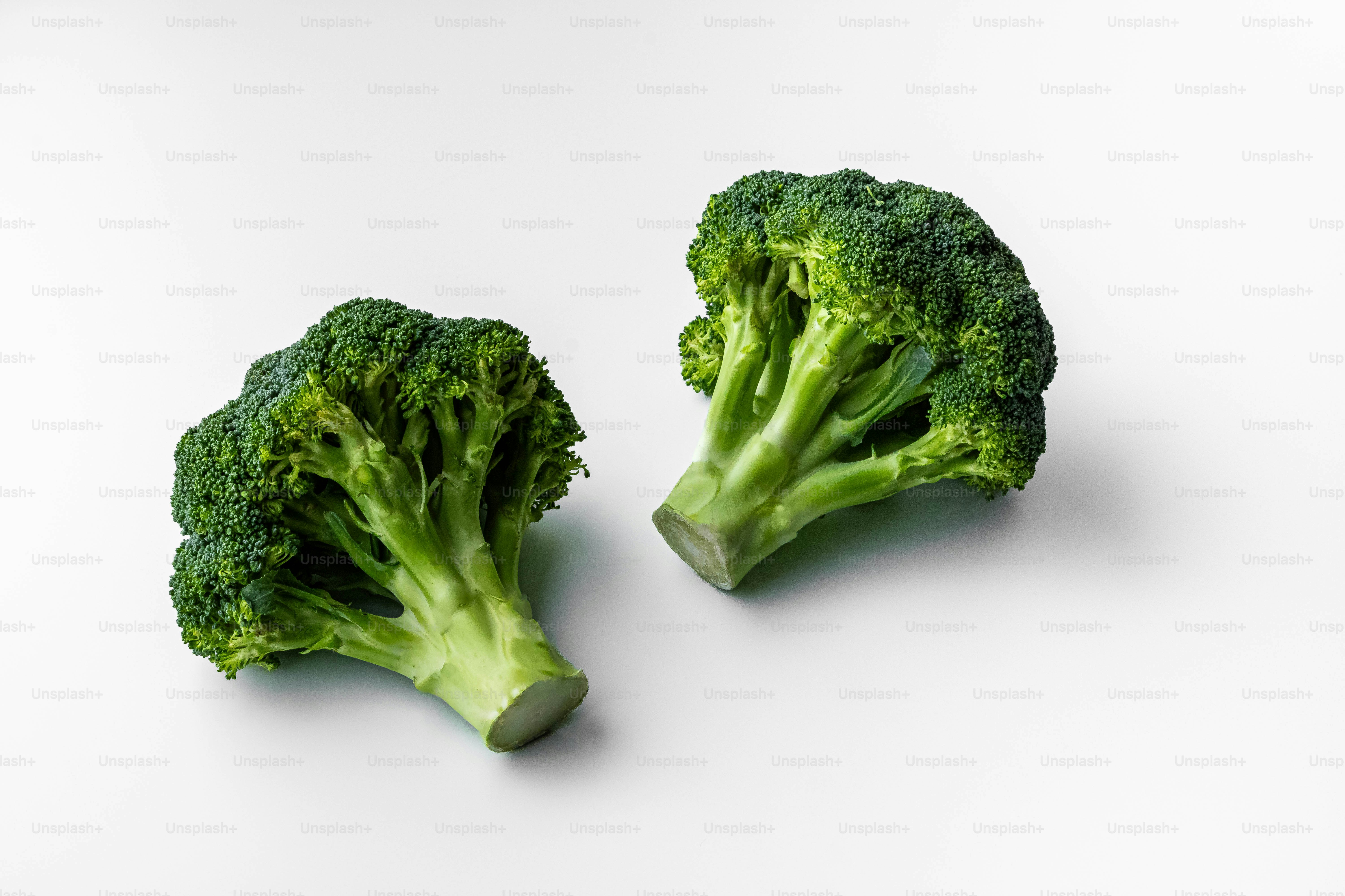 Two pieces of broccoli on a white surface