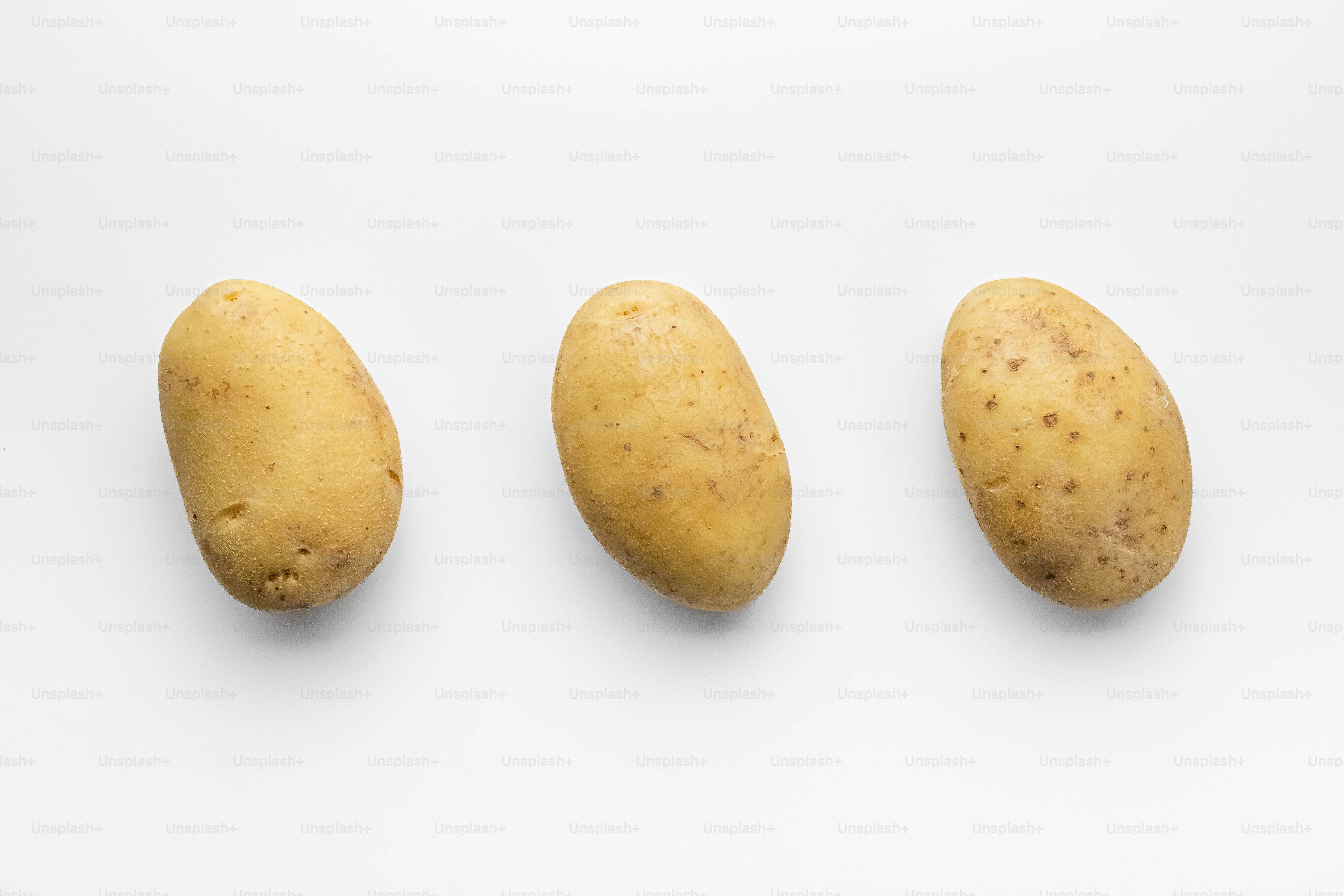 Cuatro patatas alineadas en fila sobre una superficie blanca