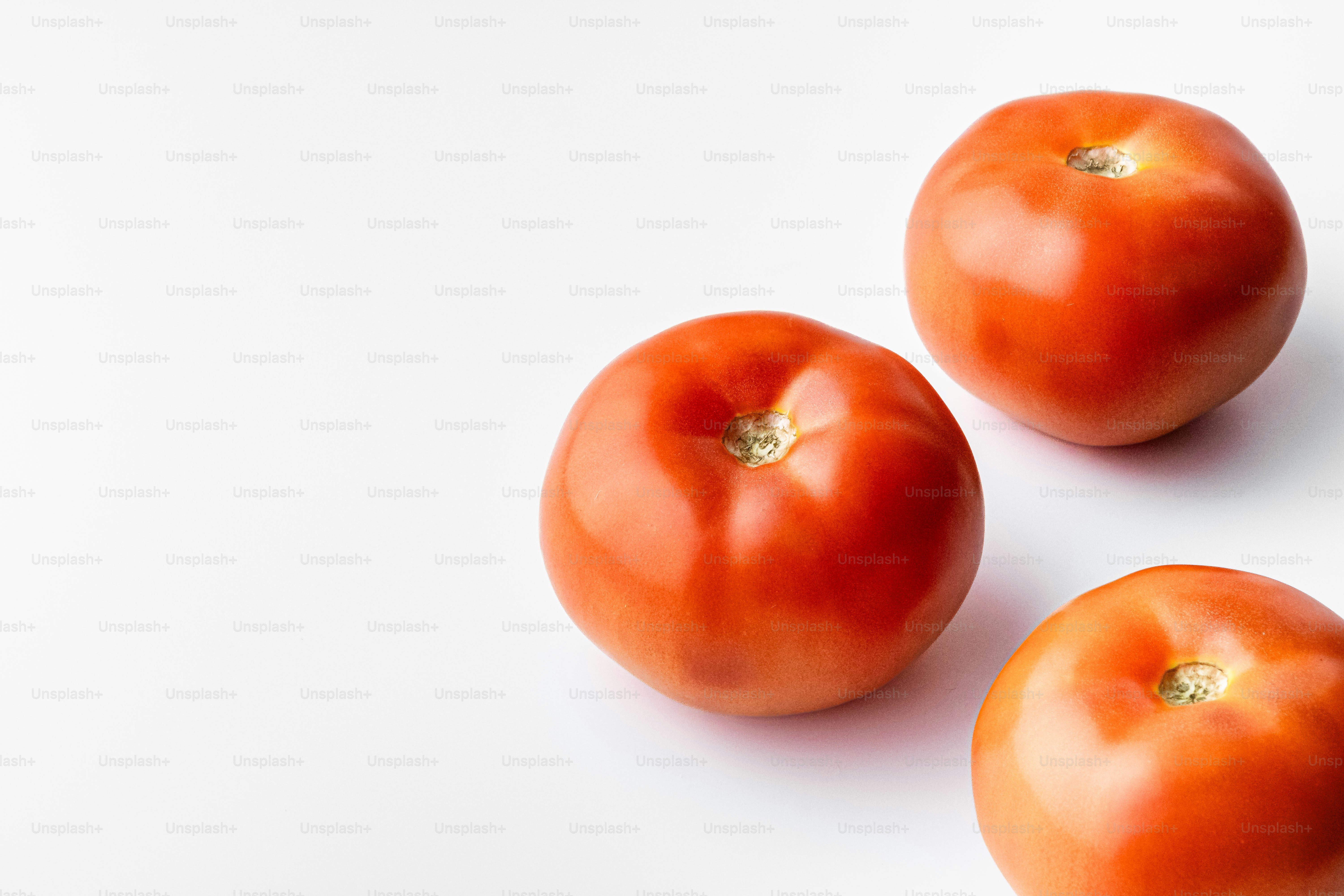 Three tomatoes on a white surface with a white background
