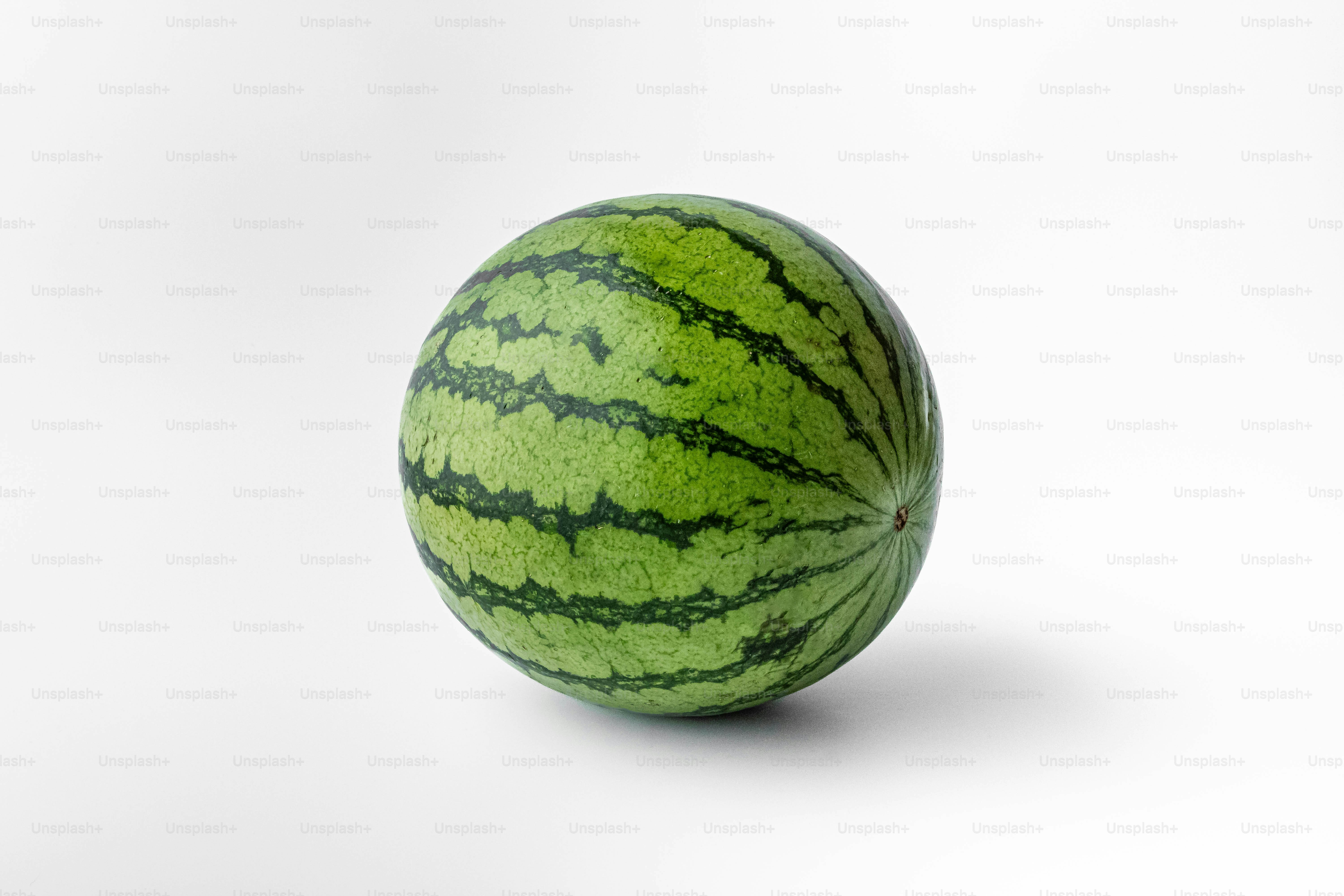 A green watermelon sitting on top of a white surface