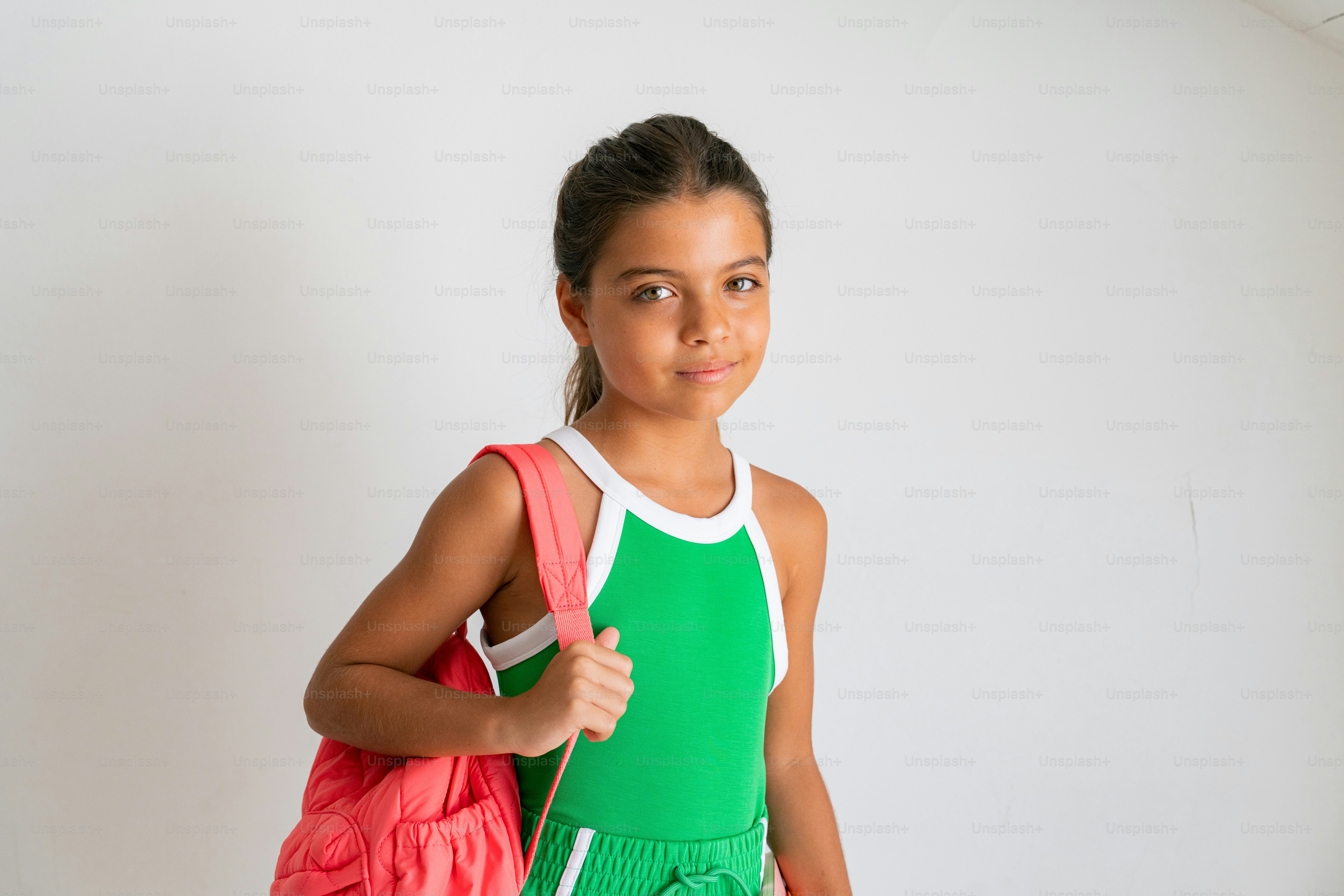 A young girl in a green and pink outfit holding a tennis racquet