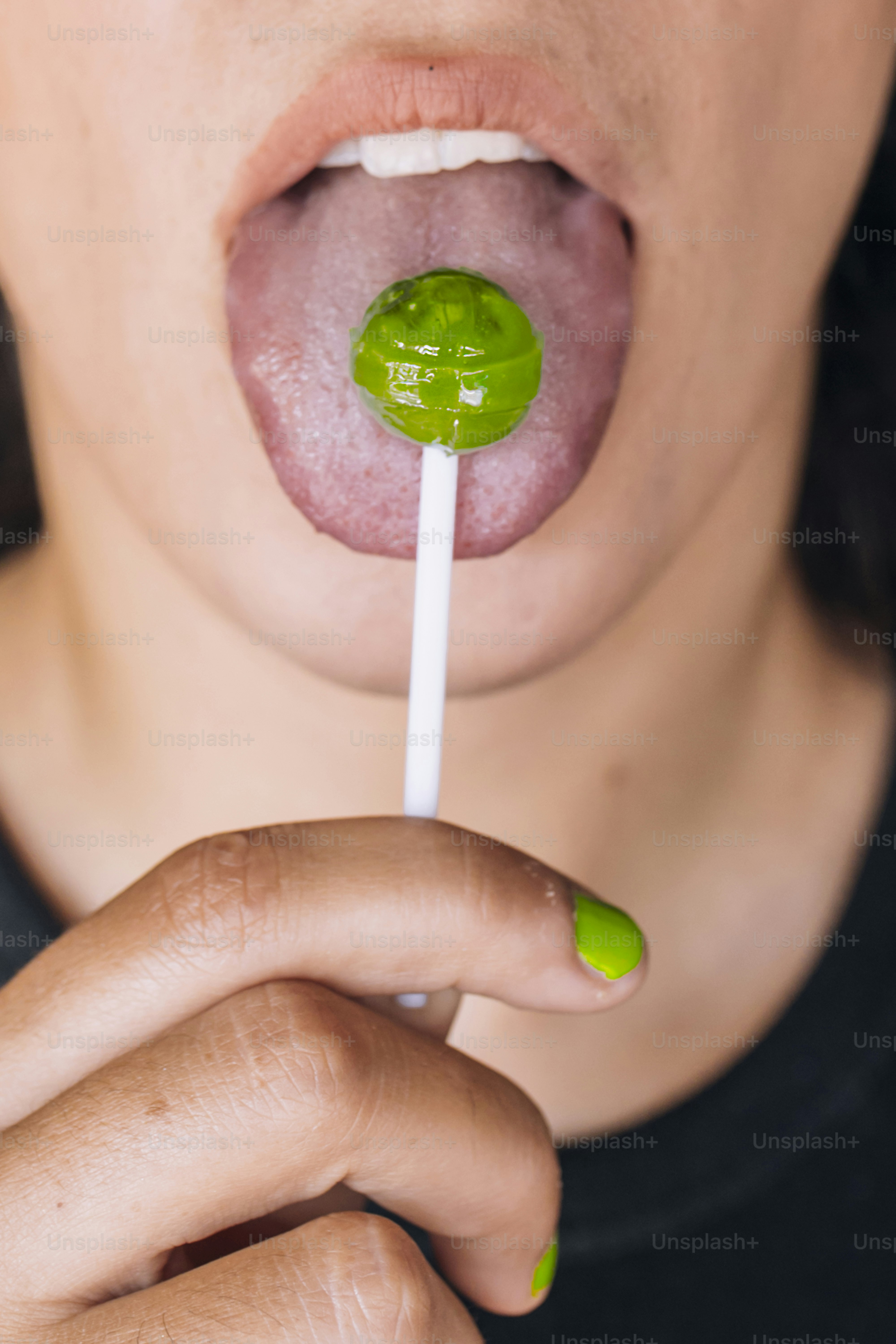 A woman holding a green lollipop in her mouth