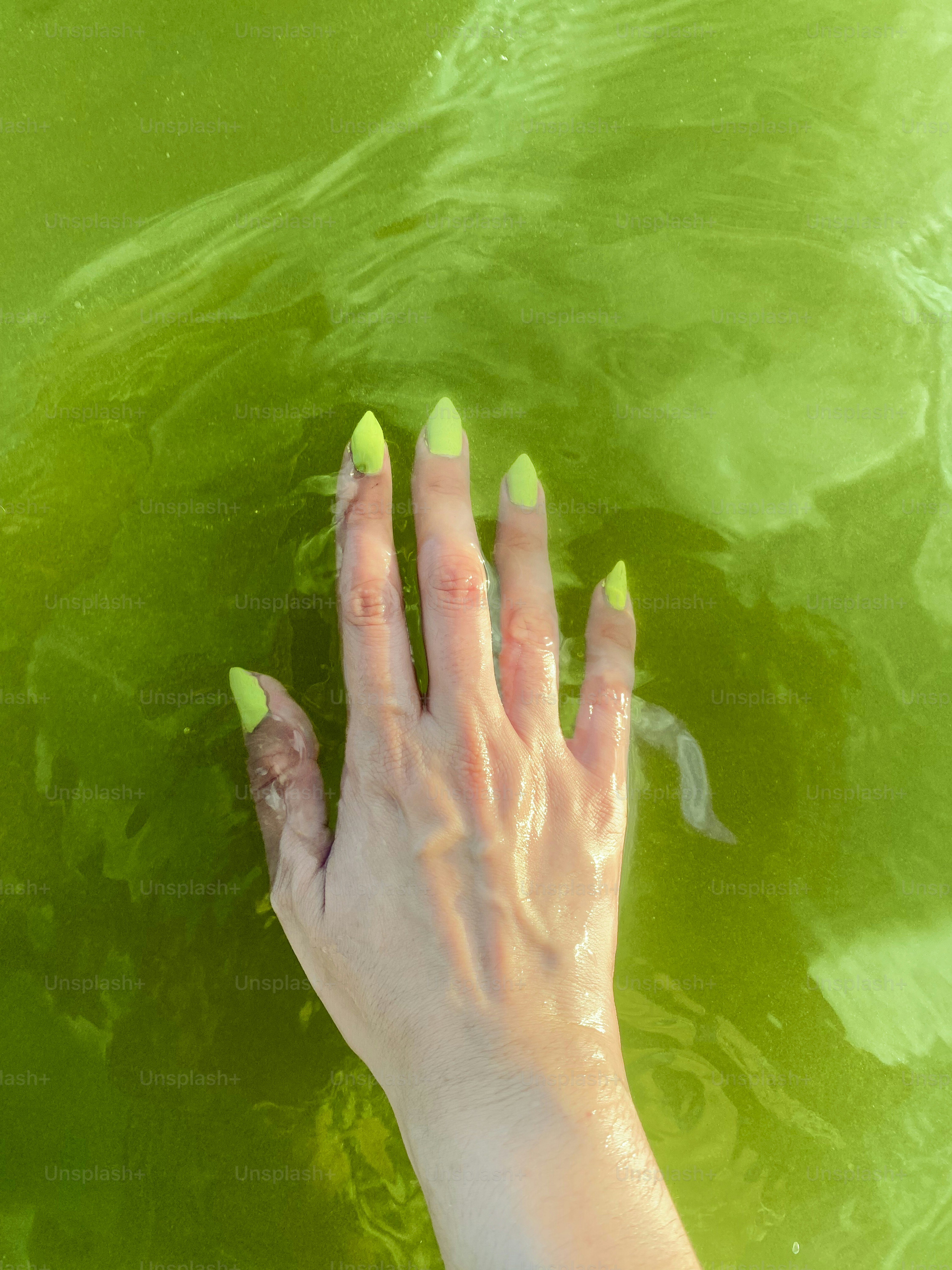 A woman's hand with green nail polish in water