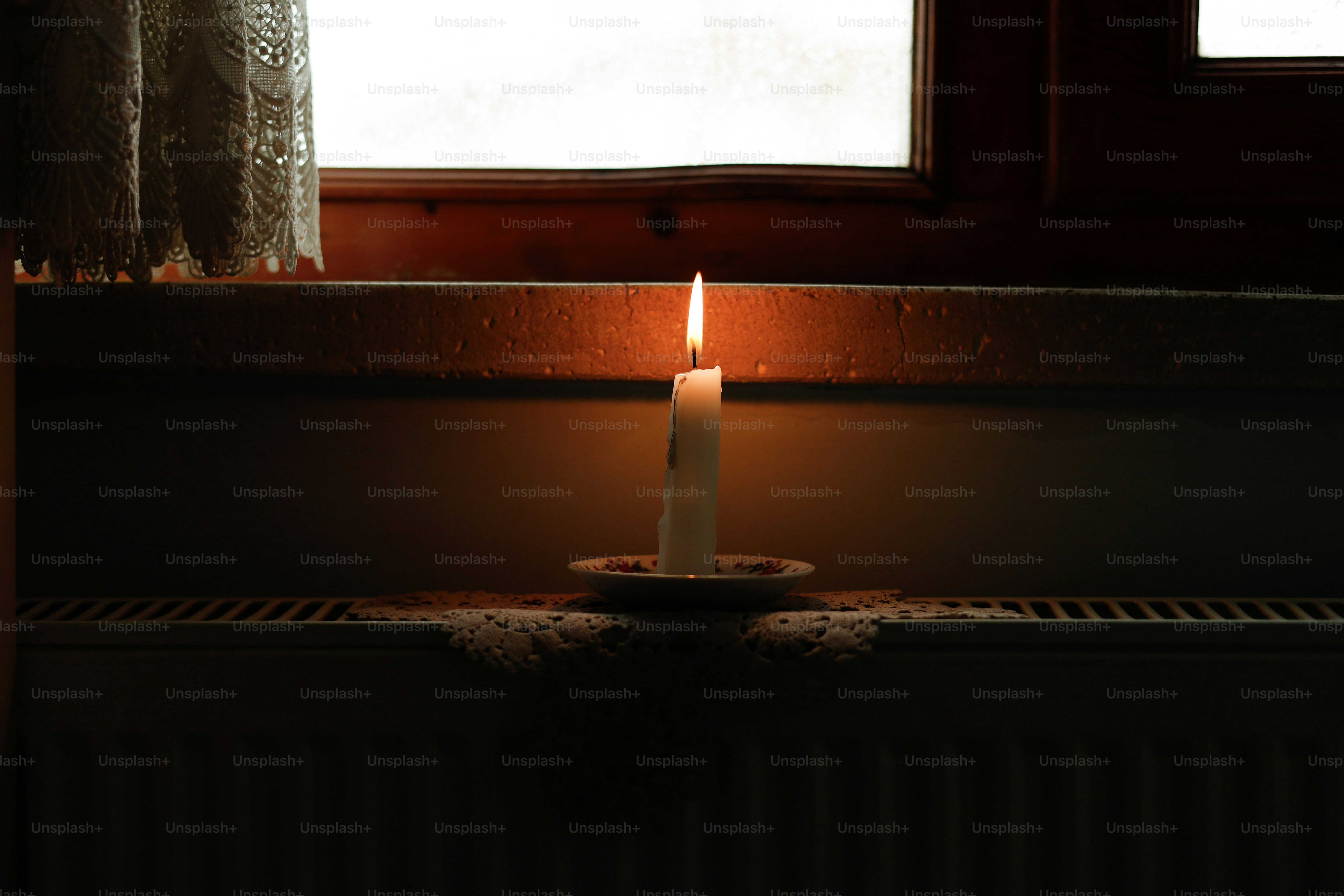 A lit candle sitting in front of a window