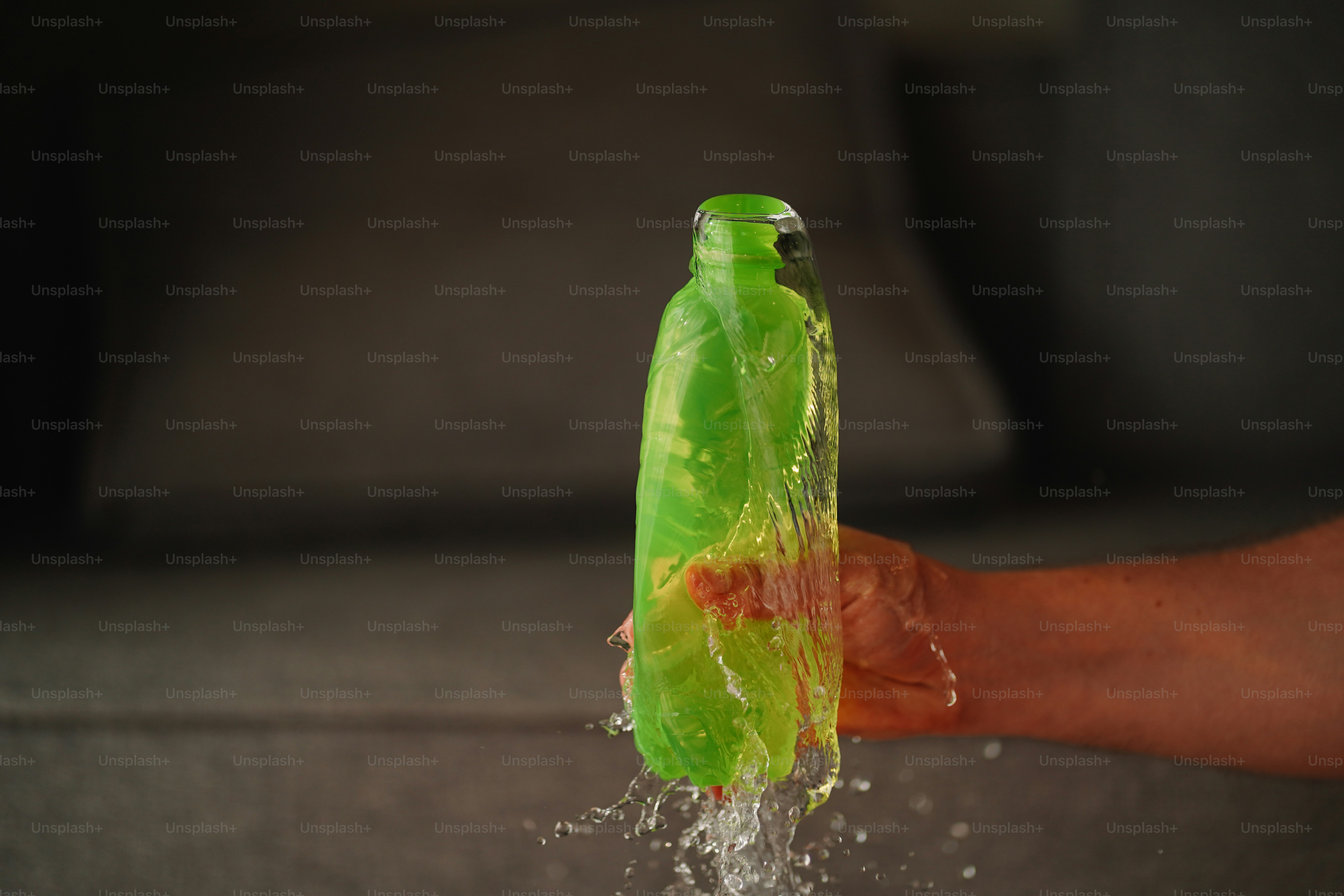 A person's hand holding a green bottle with water coming out of it