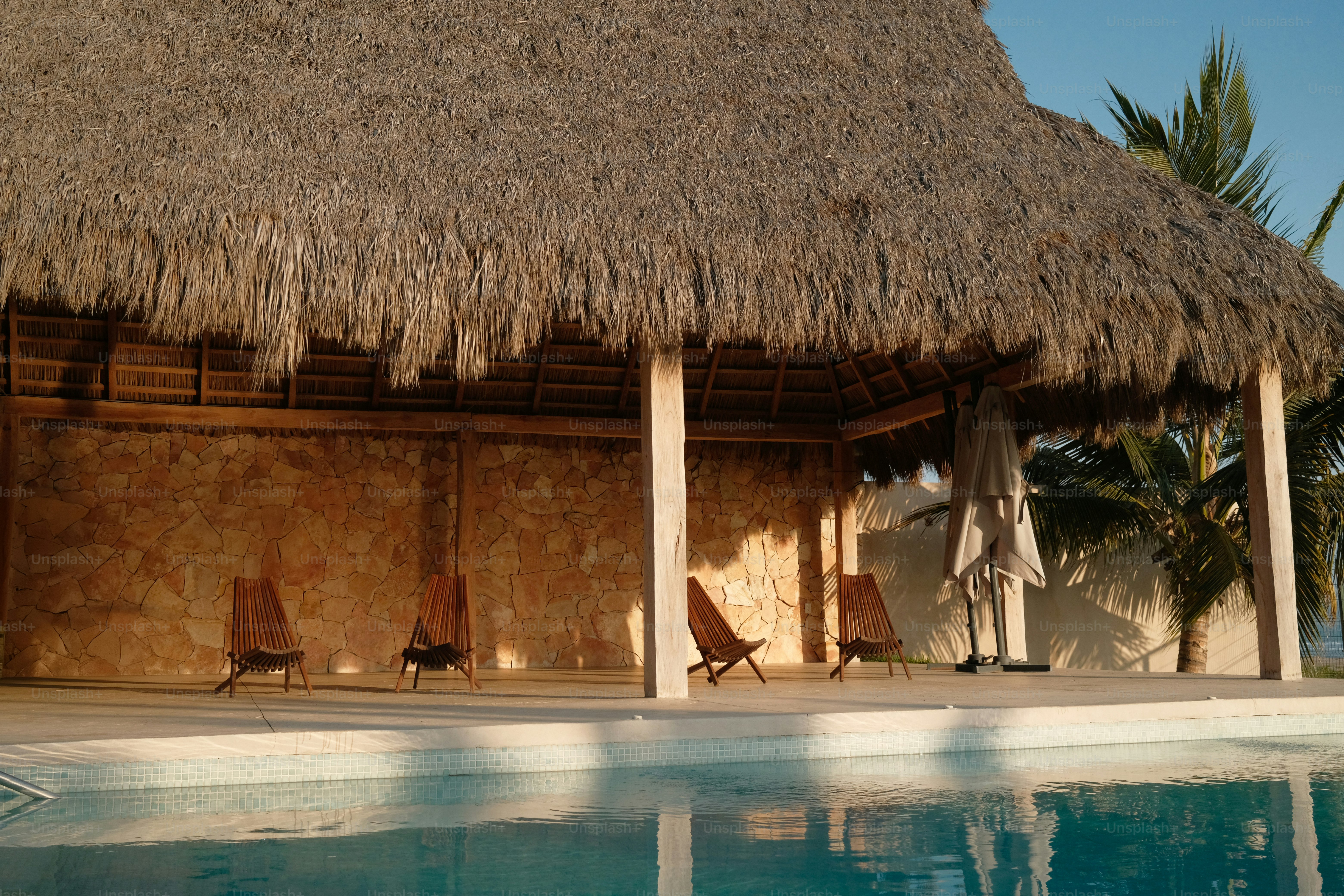 A hut with a thatched roof next to a swimming pool
