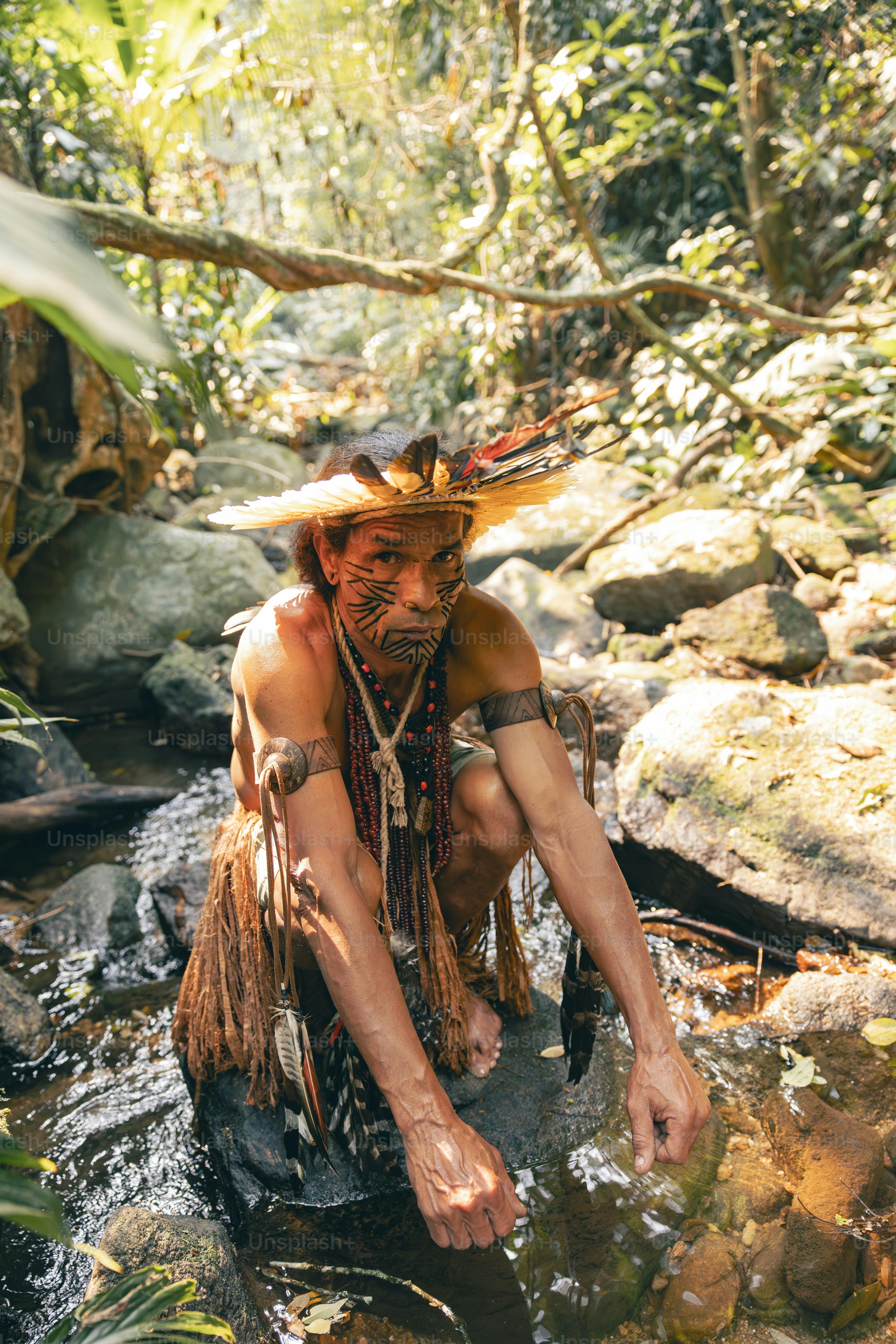 A man in a native american headdress crouches in a stream