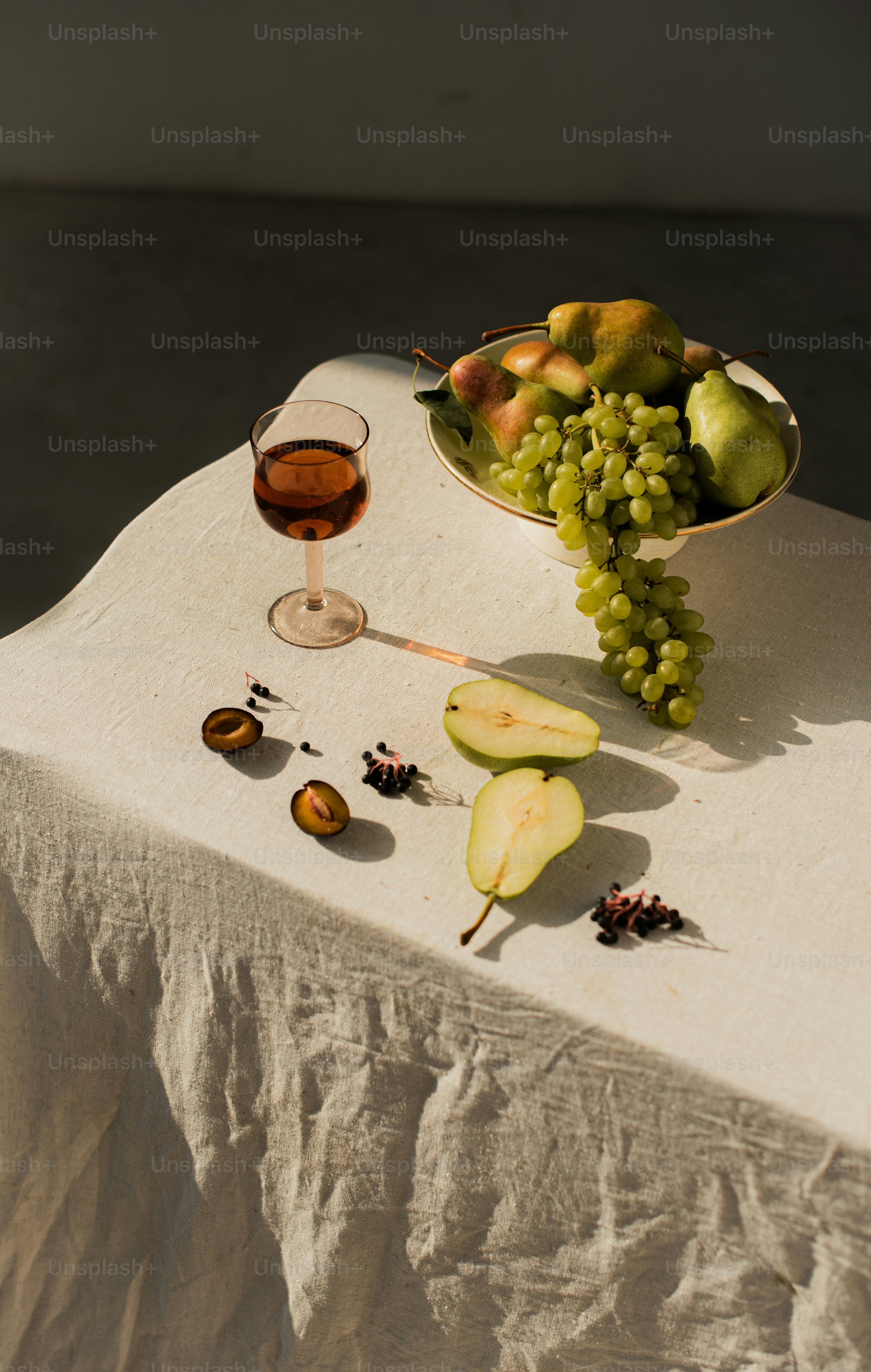 A table topped with a bowl of fruit and a glass of wine