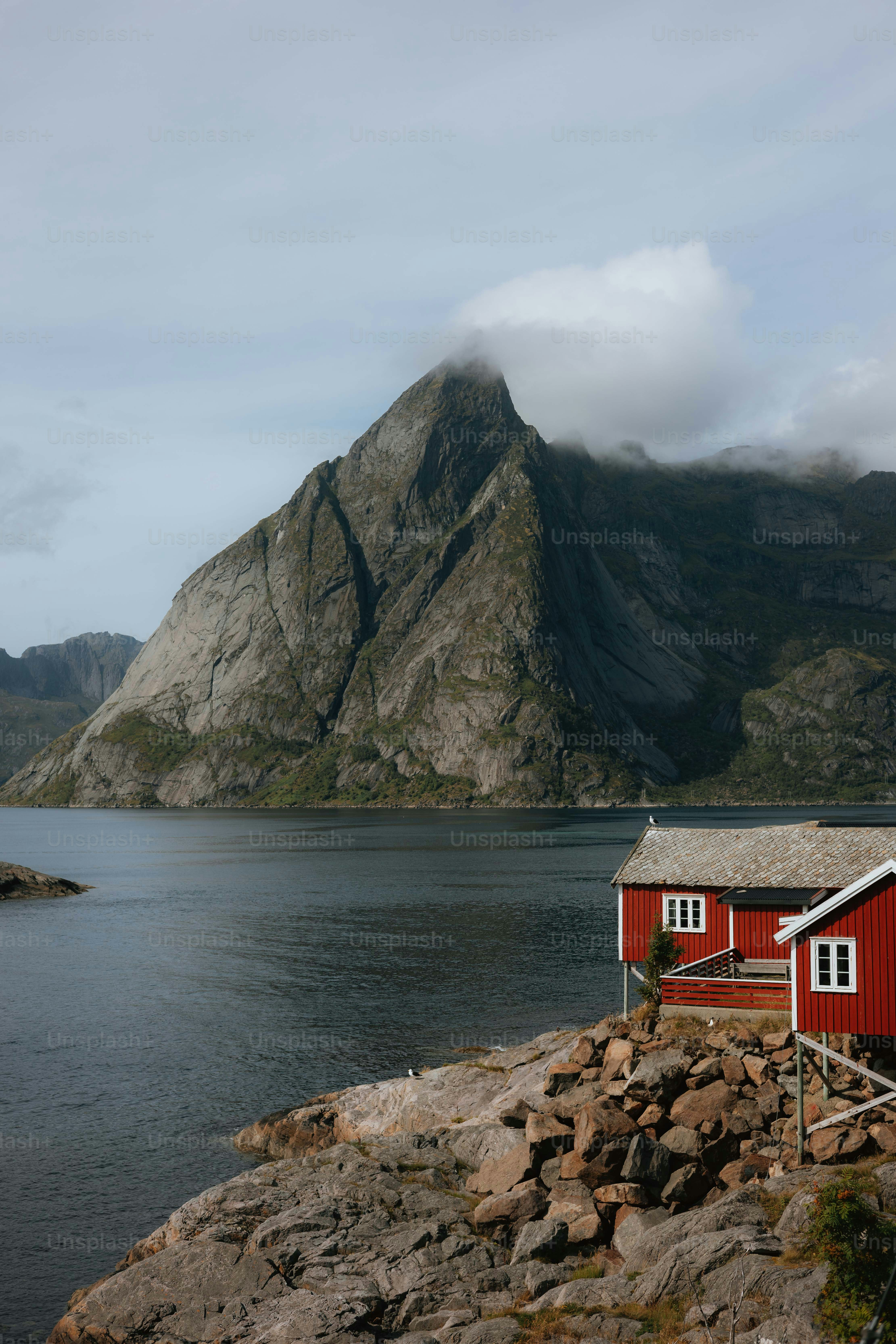 A red house sitting on top of a rocky hill next to a body of water