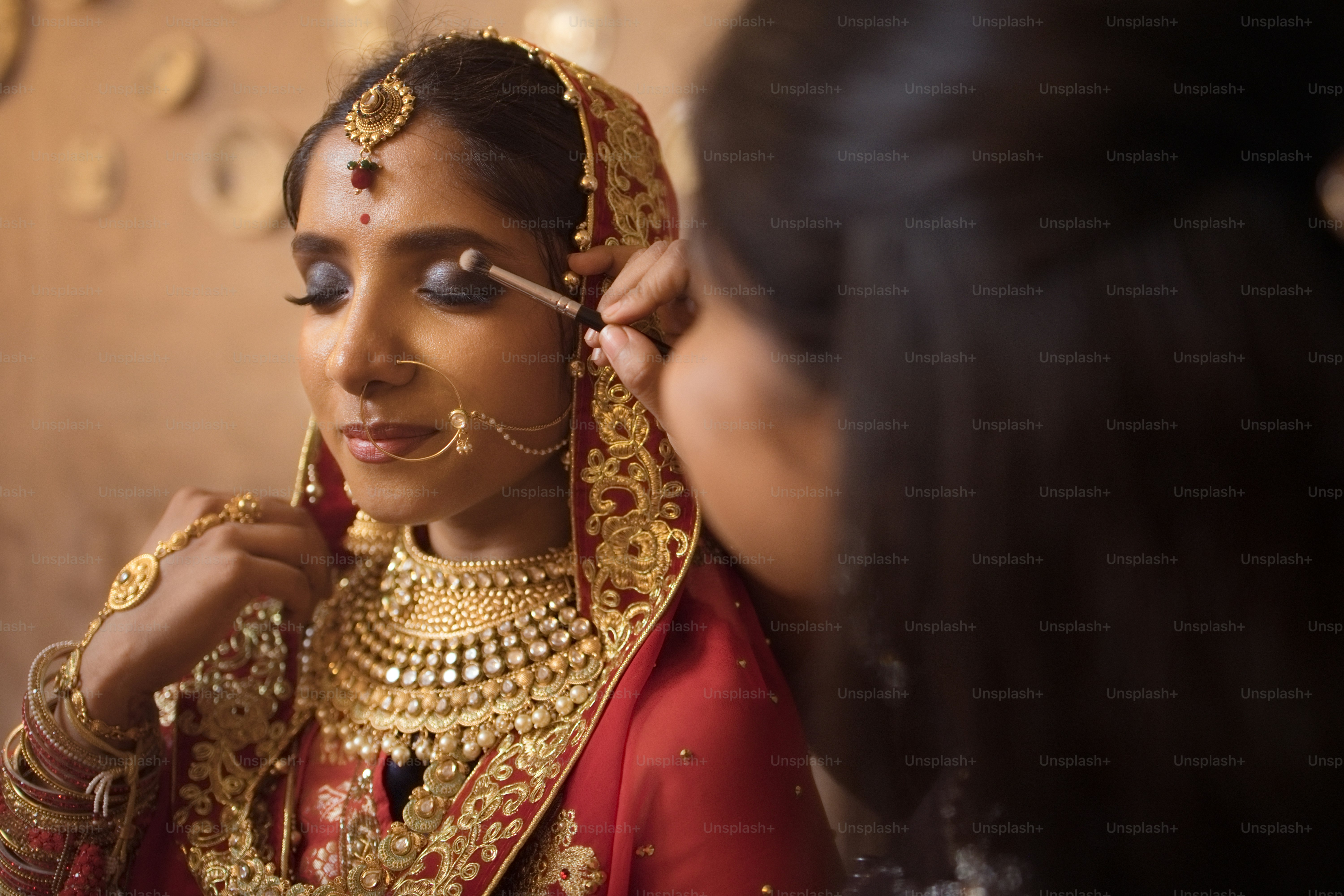 Une femme en mariée rouge et or se fait maquiller