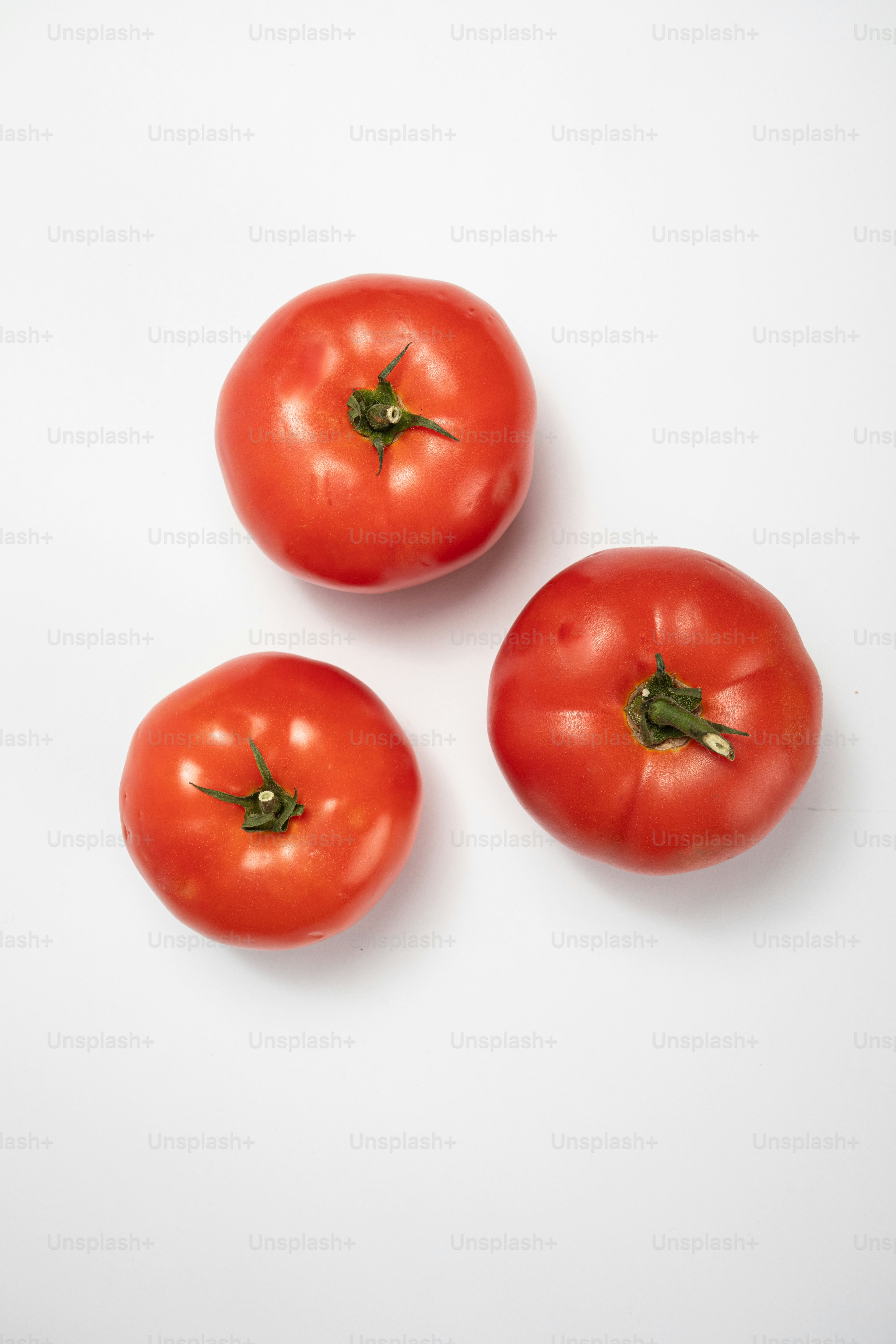 Three red tomatoes on a white surface
