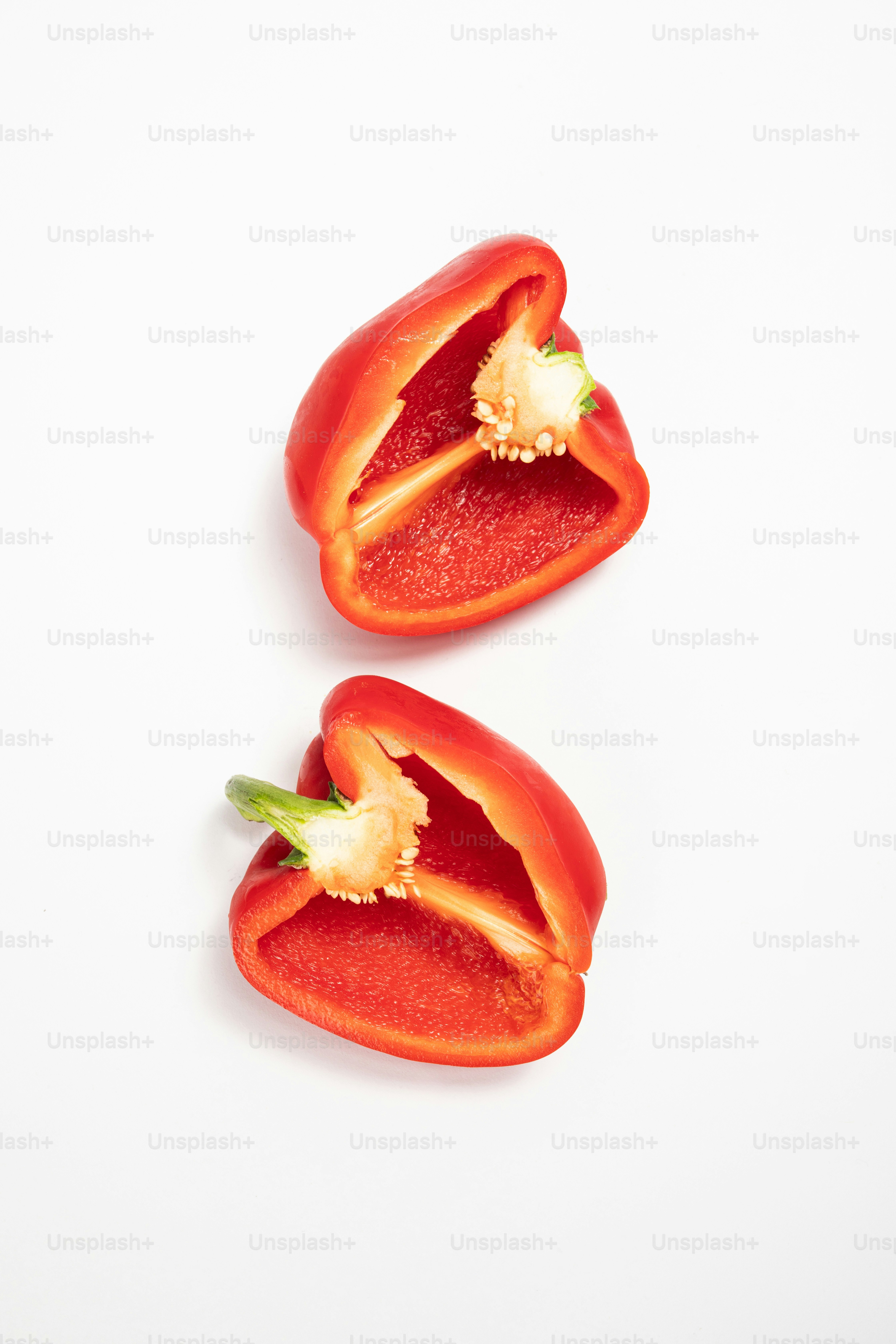 Dos pimientos rojos cortados por la mitad sobre una superficie blanca