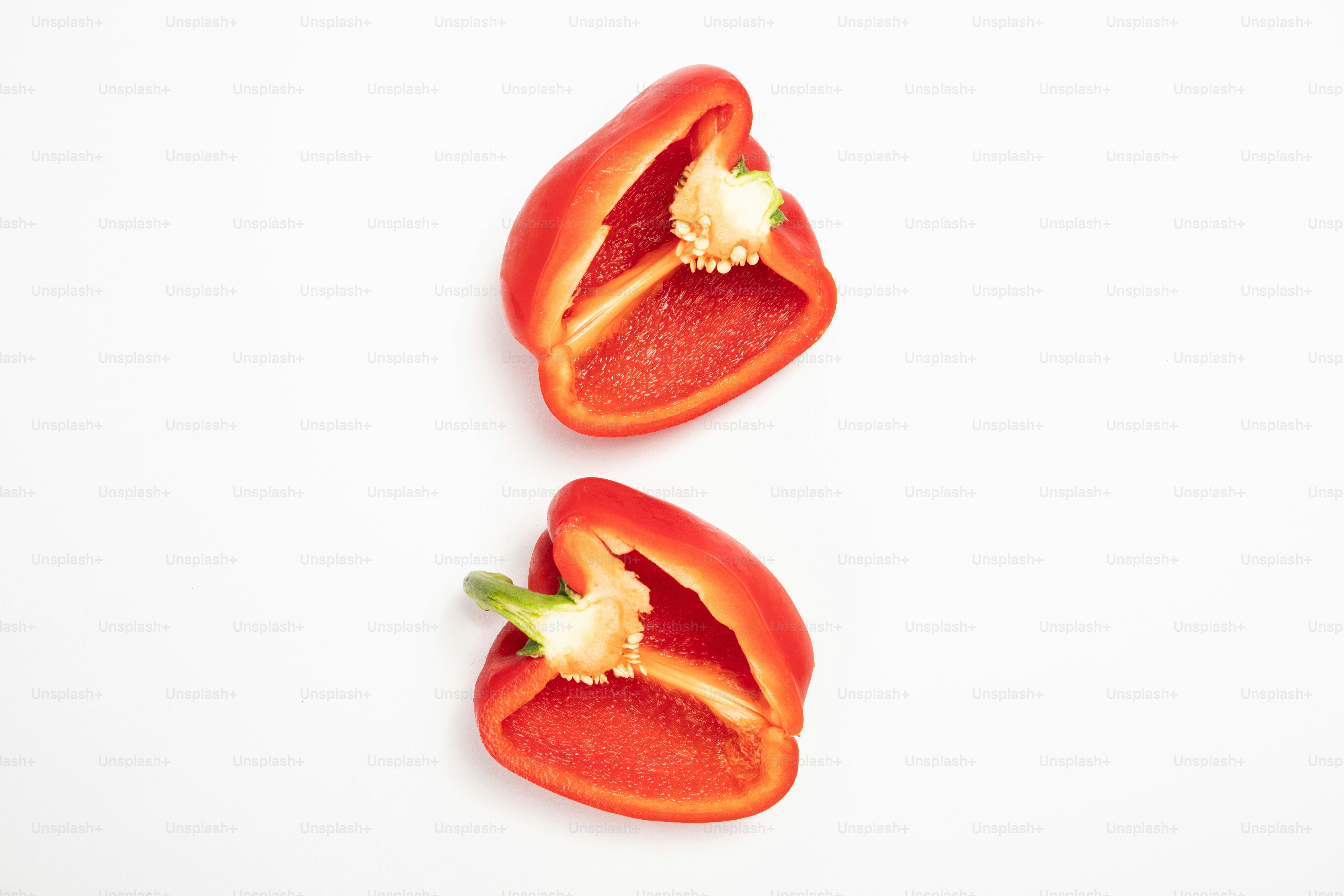 Dos pimientos rojos cortados por la mitad sobre una superficie blanca