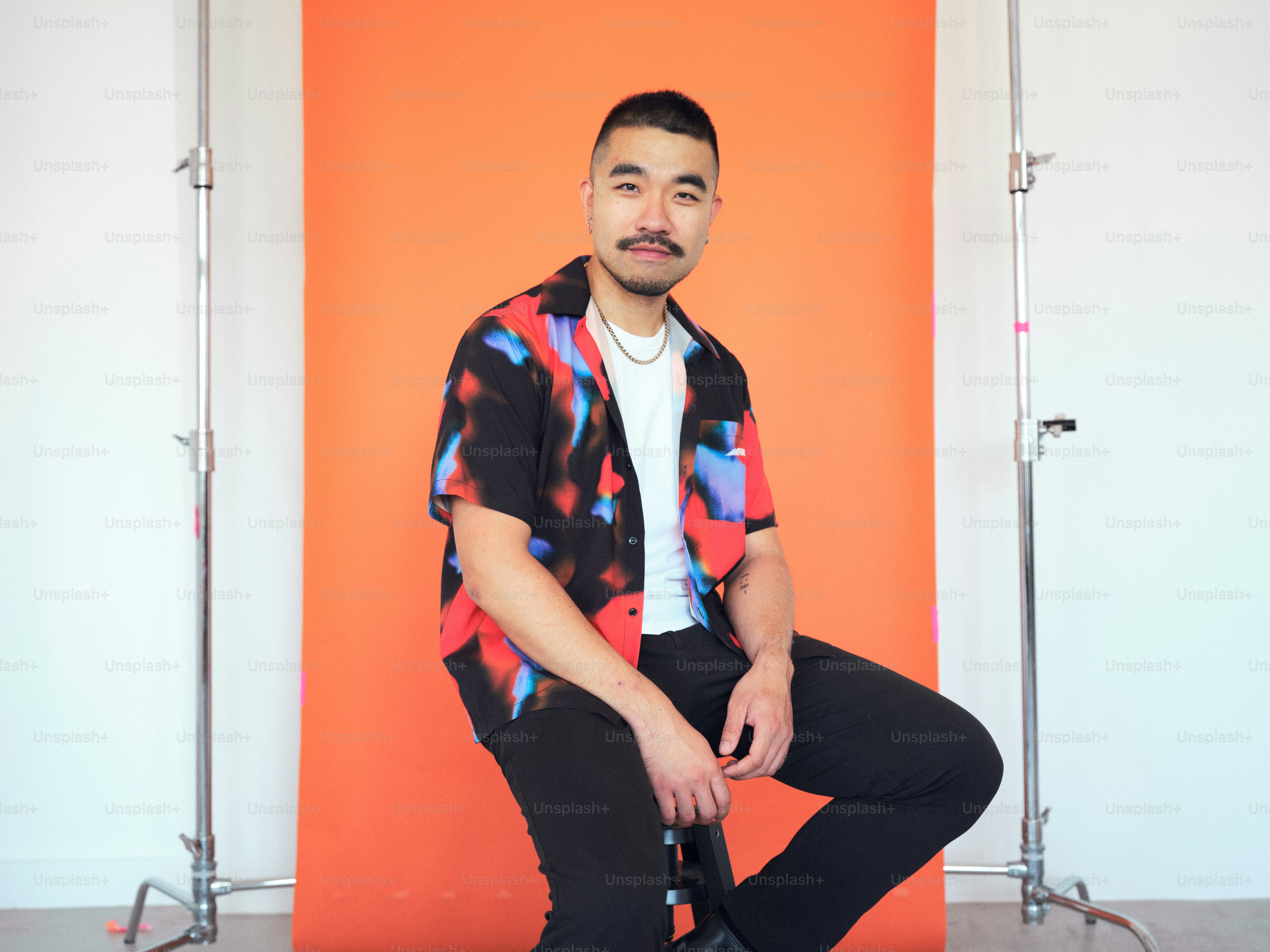 A man sitting on a stool in front of an orange wall
