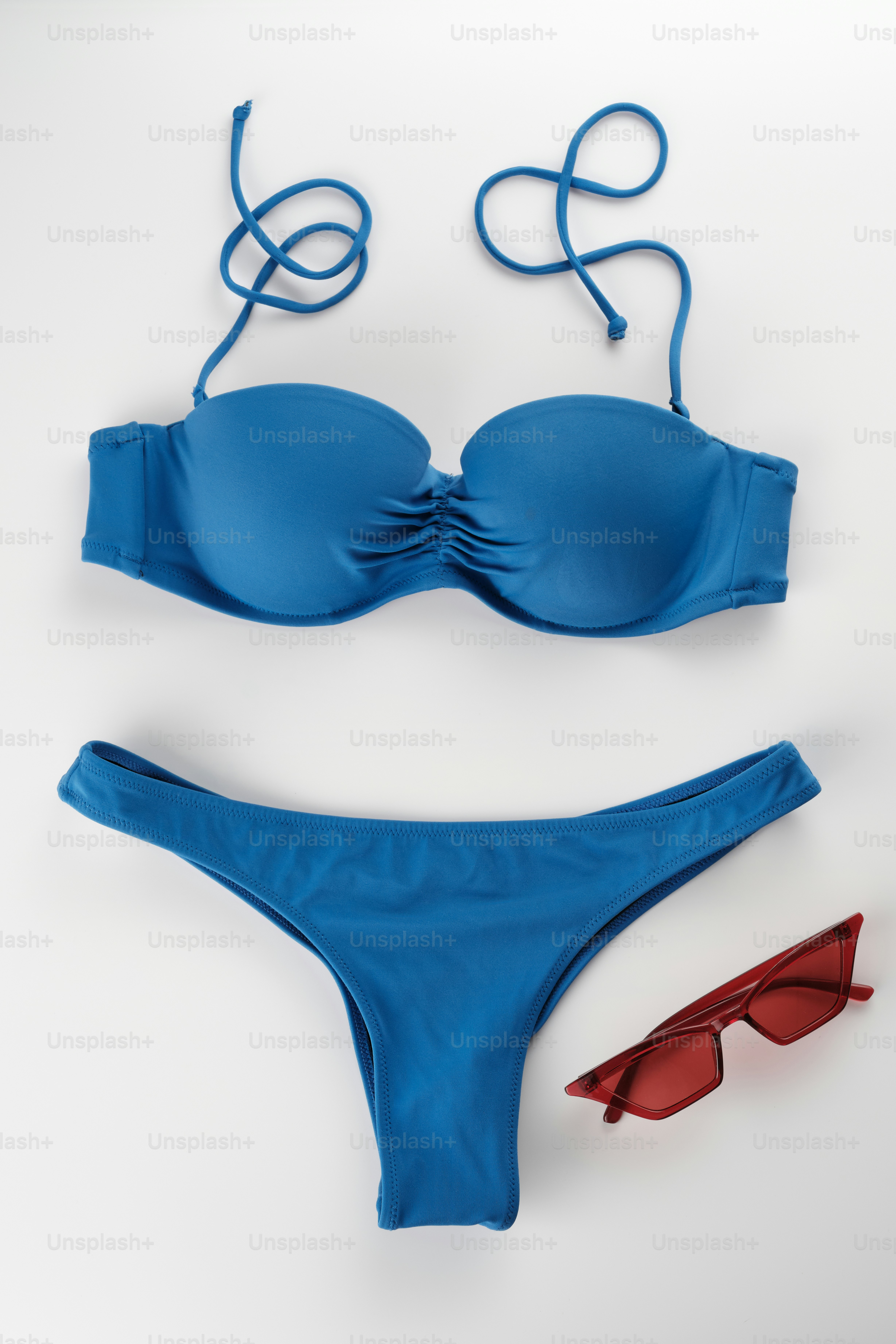 A blue bikini and red sunglasses on a white surface