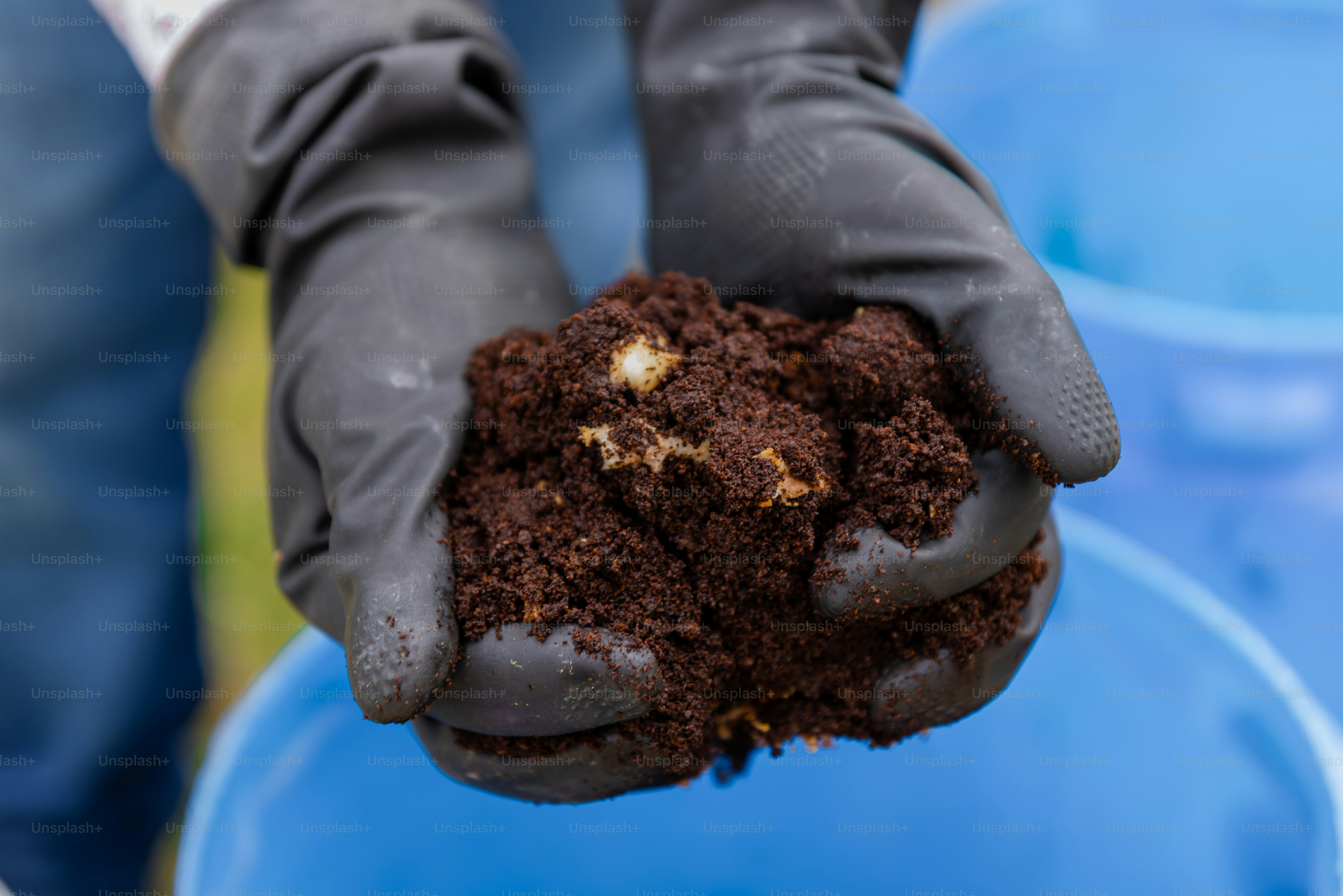 A person holding a blue bucket filled with dirt