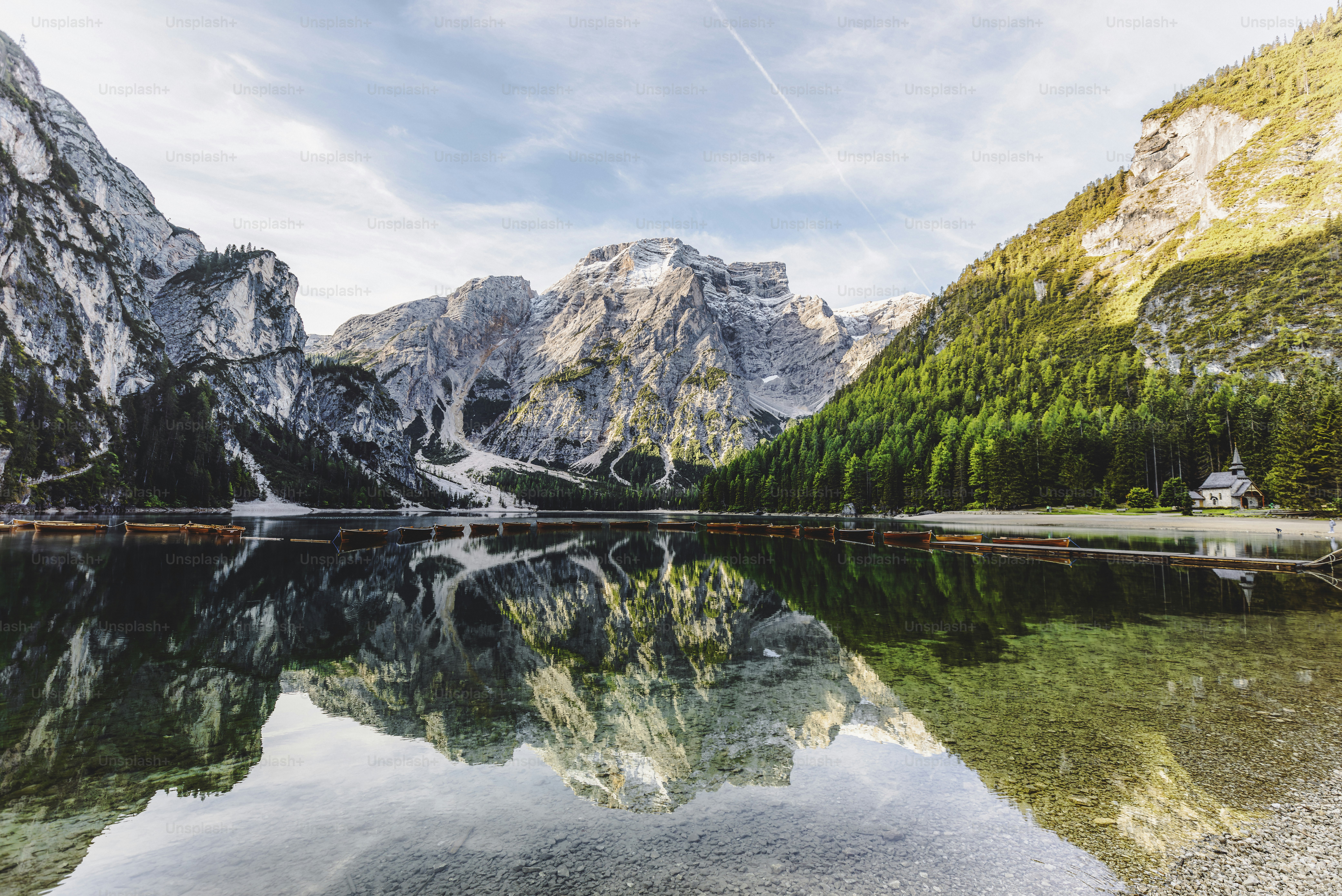 Beautiful lake in nature and summer with a wooden pier, orange boats and mountain reflection during sunrise at a beautiful turquoise water lake Lago di Braies, Trentino Alto Adige, South Tirol, European Alps, Italia, South Europe