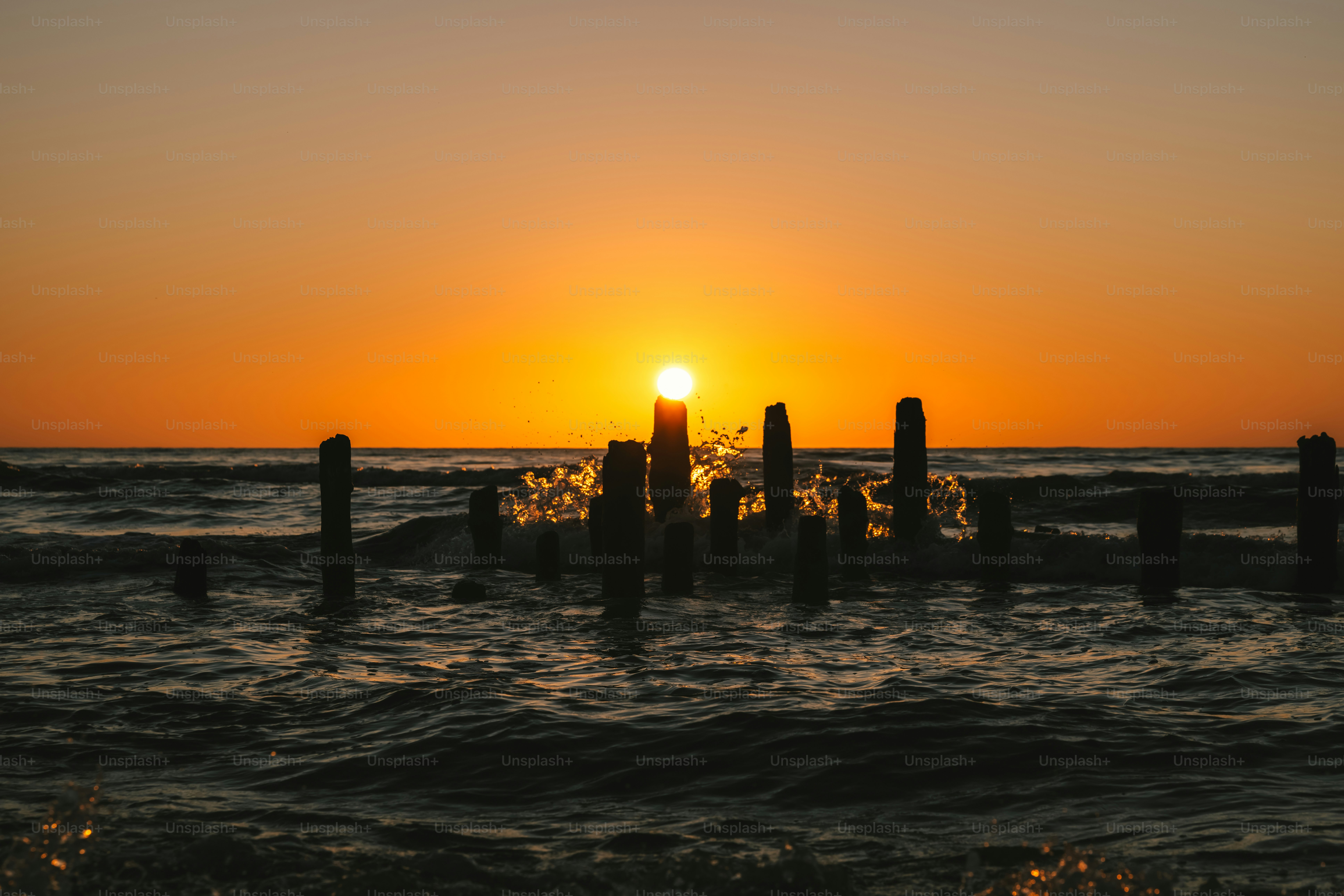 The sun is setting over the ocean with a pier in the foreground