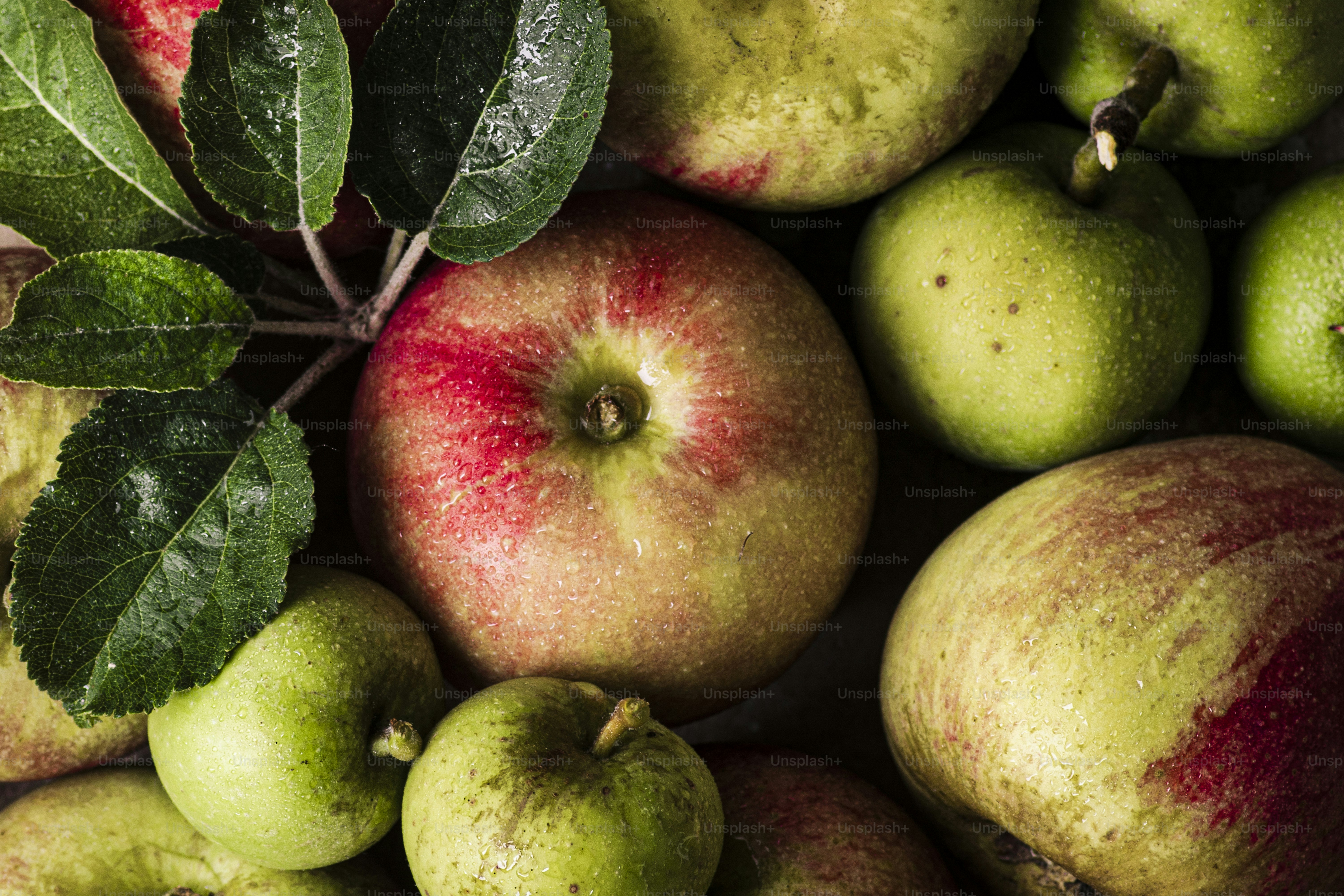 A pile of green and red apples with leaves
