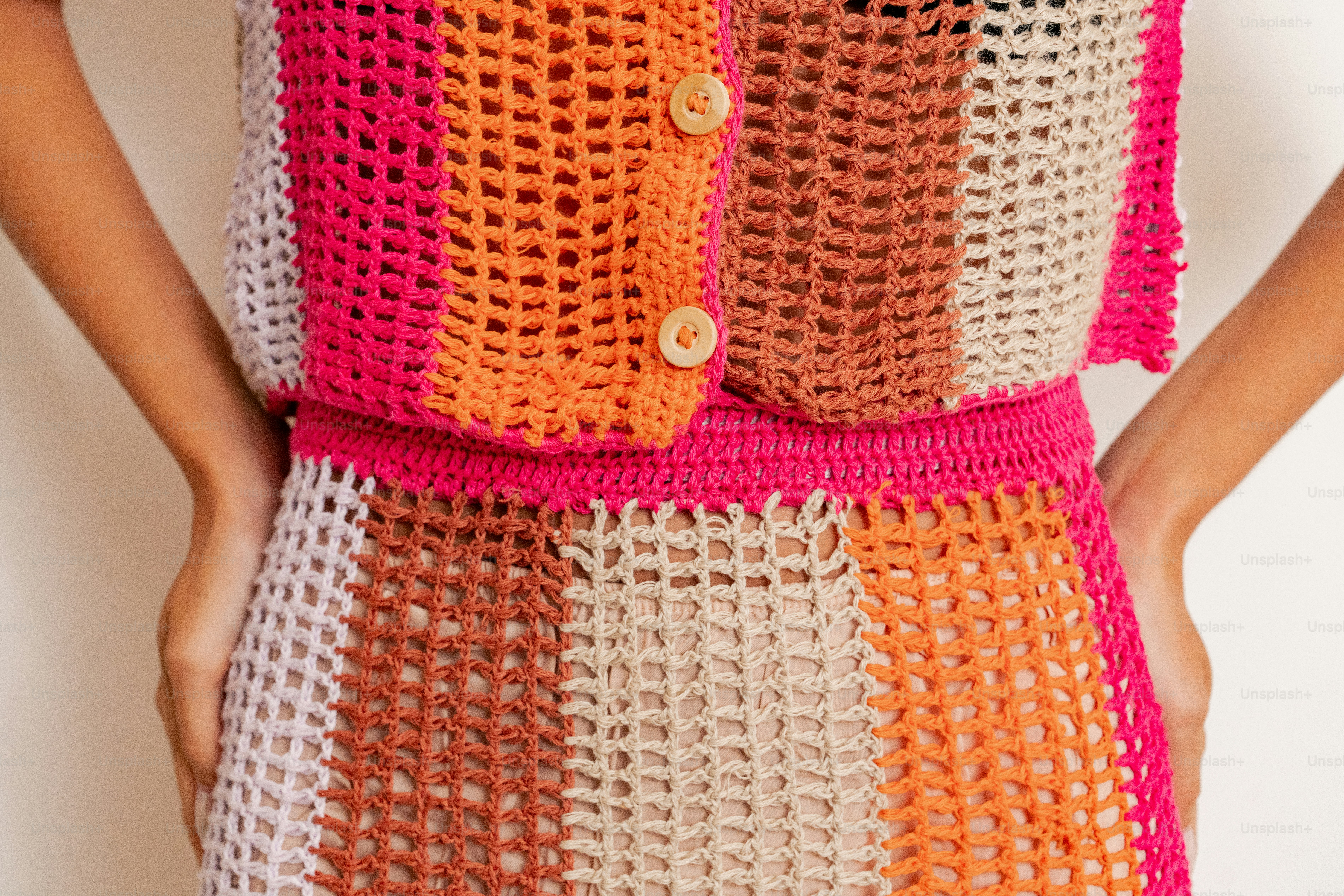 A woman is wearing a crocheted dress with a pink, orange, and