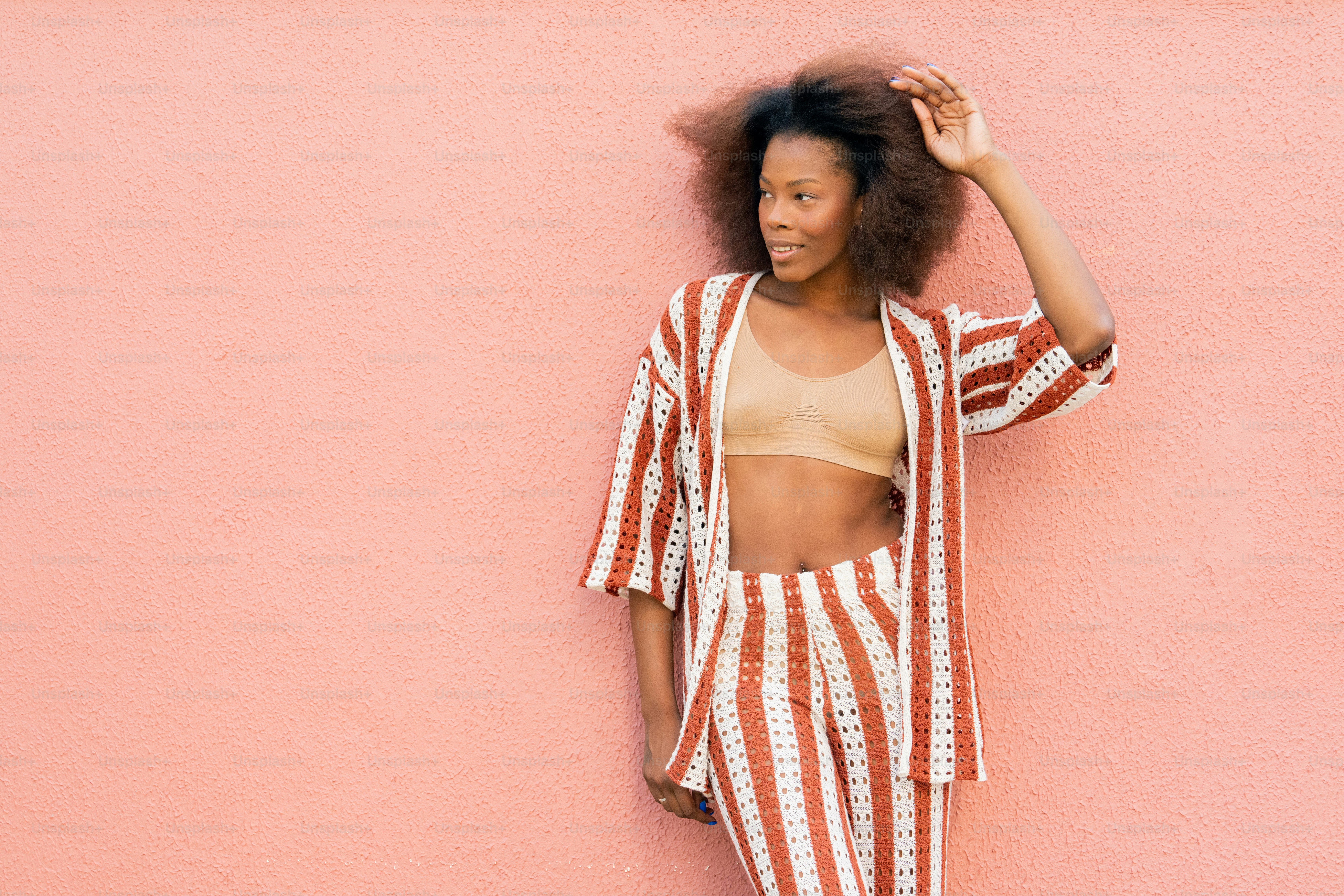 A woman leaning against a pink wall with her hair in the air