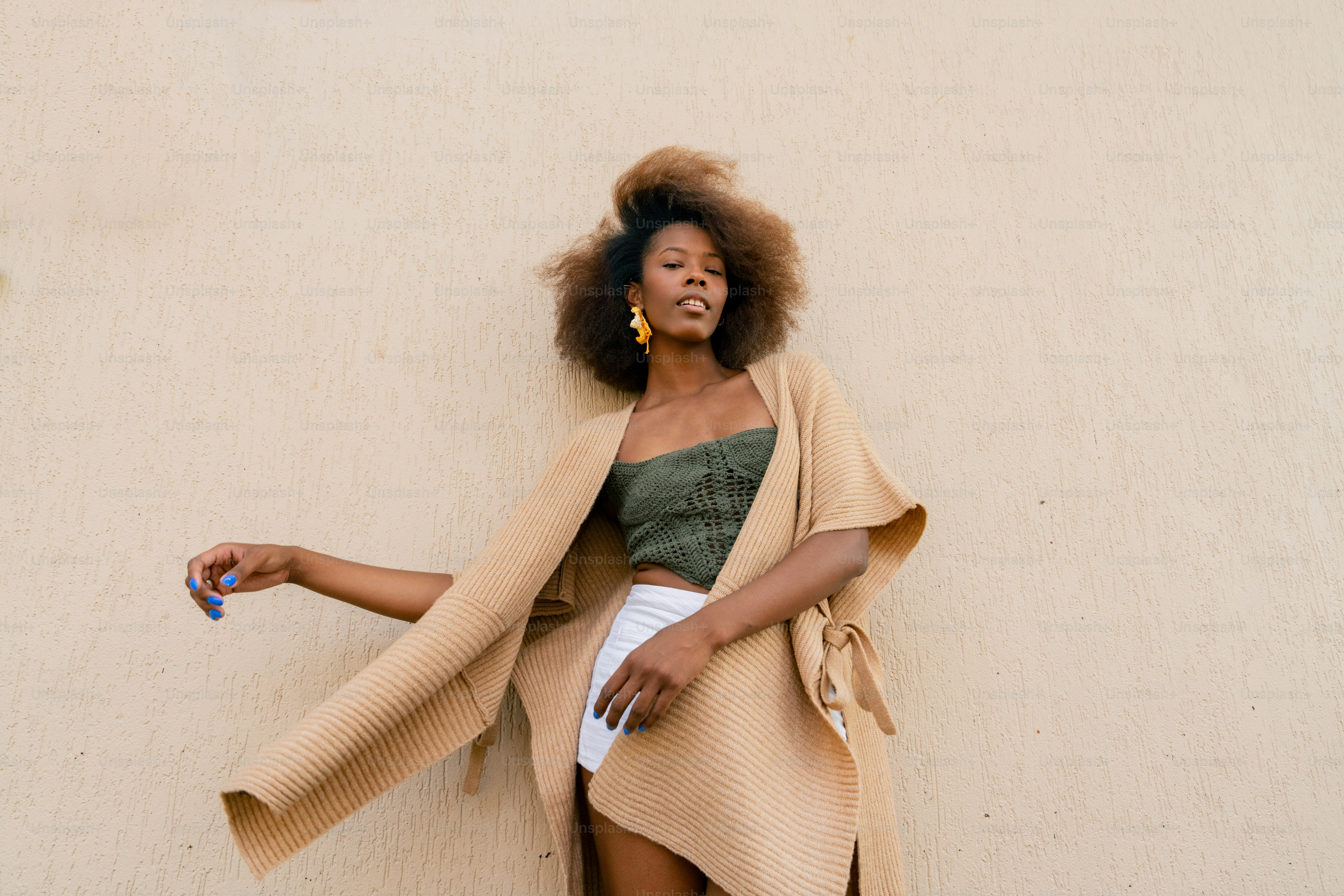 A woman leaning against a wall wearing a tan coat