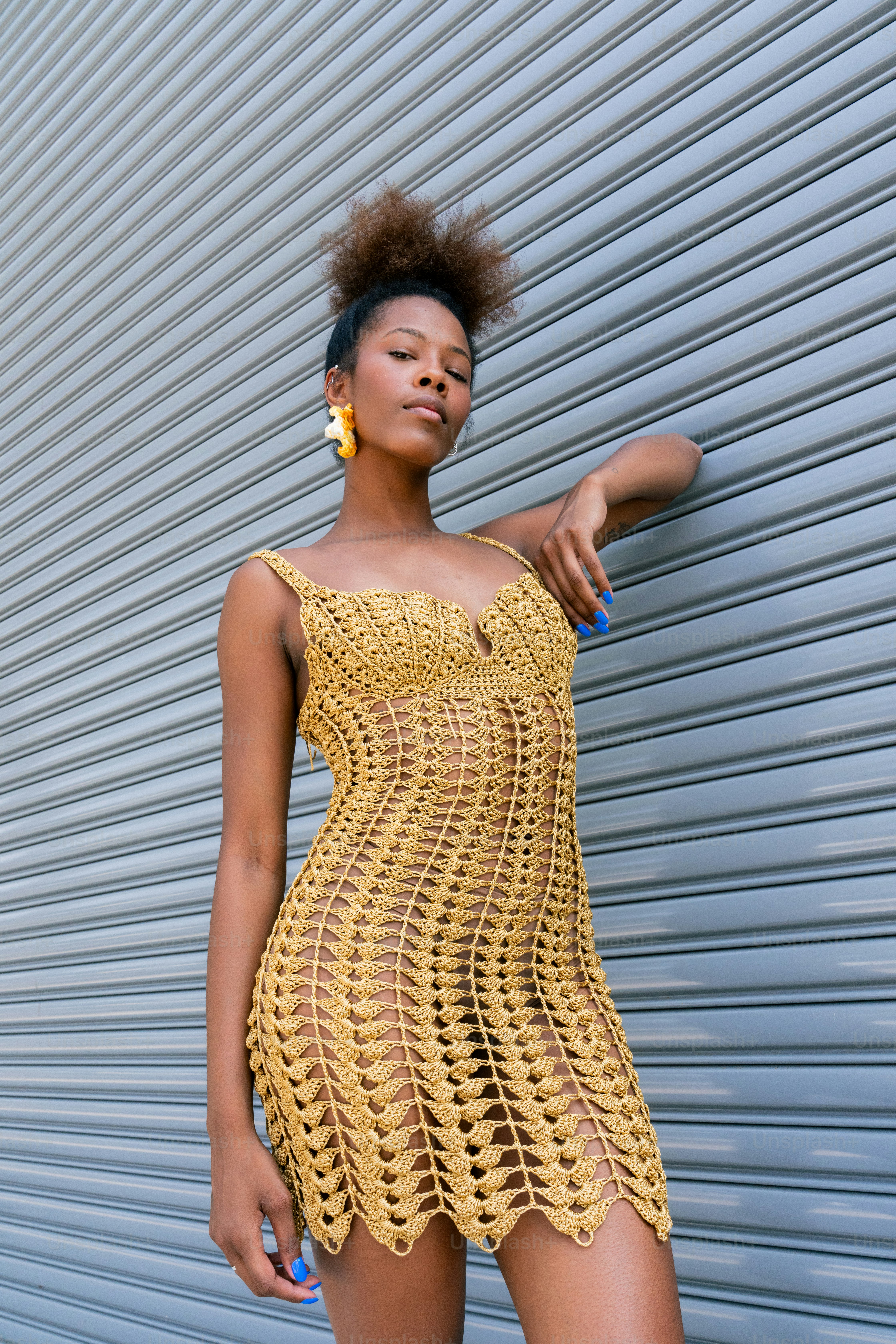 A woman in a yellow crochet dress leaning against a wall