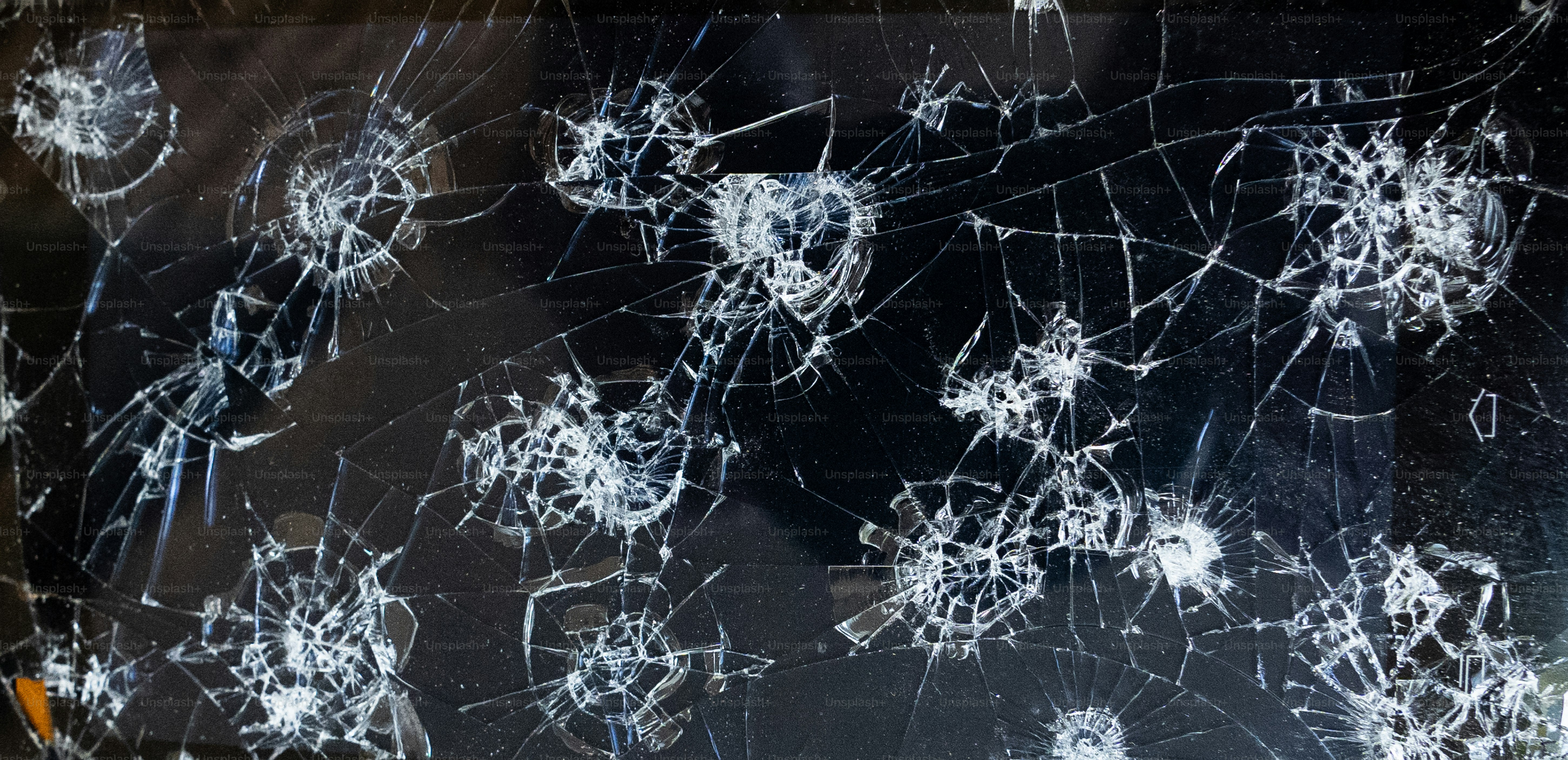 A broken glass window with a bunch of bullet holes