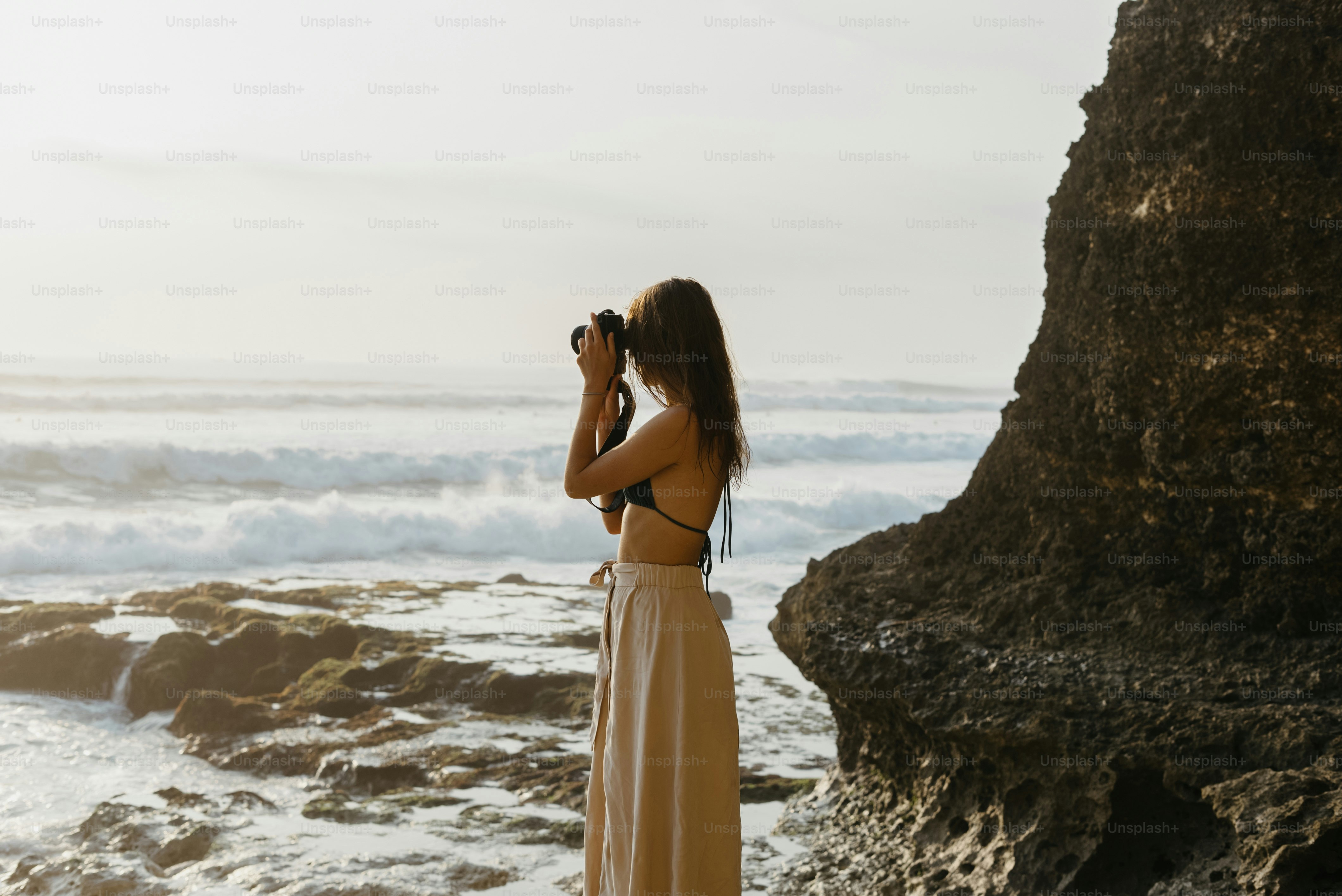 A woman standing on a beach taking a picture of the ocean