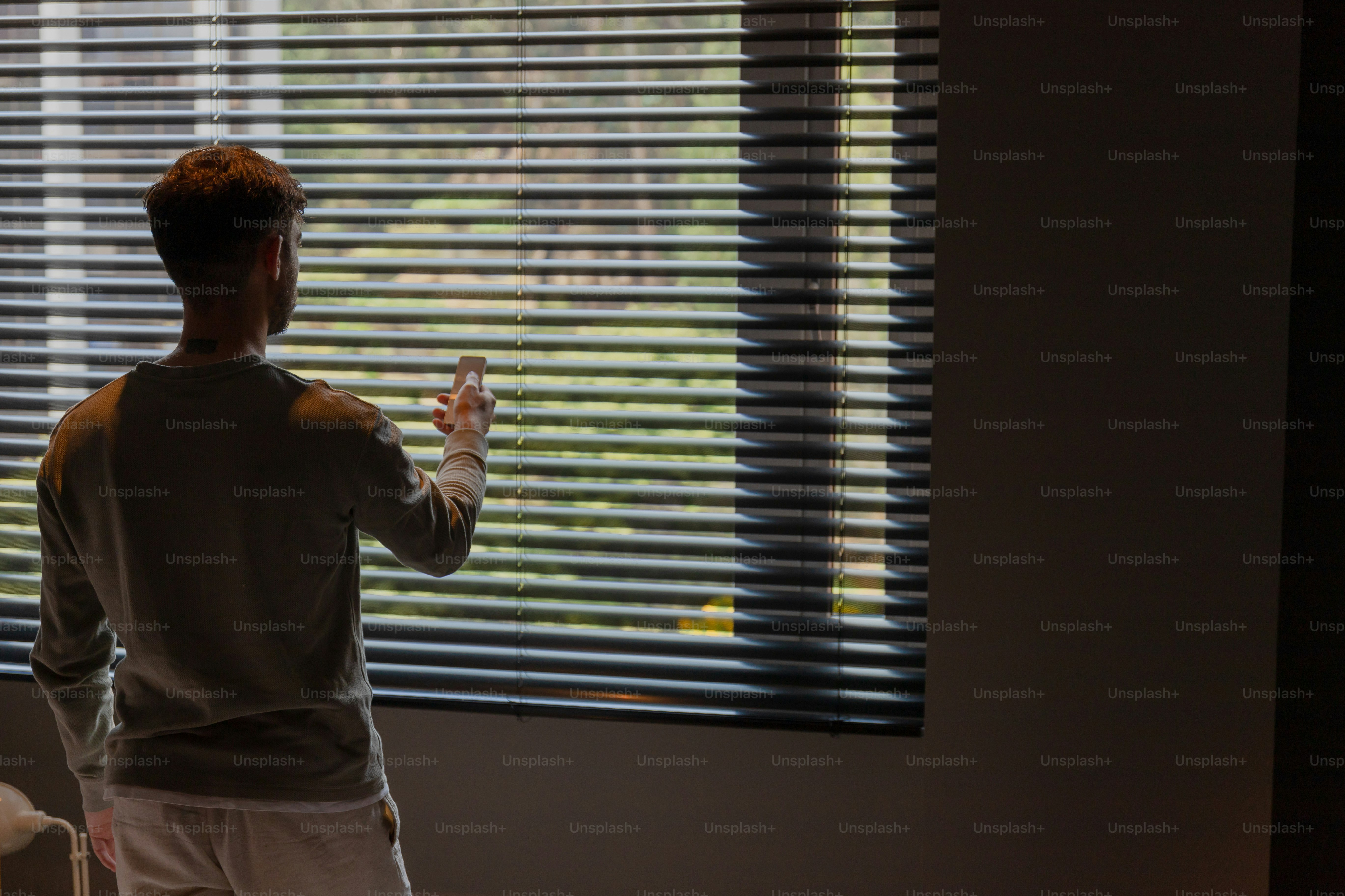 A man standing in front of a window with blinds photo – Technology ...
