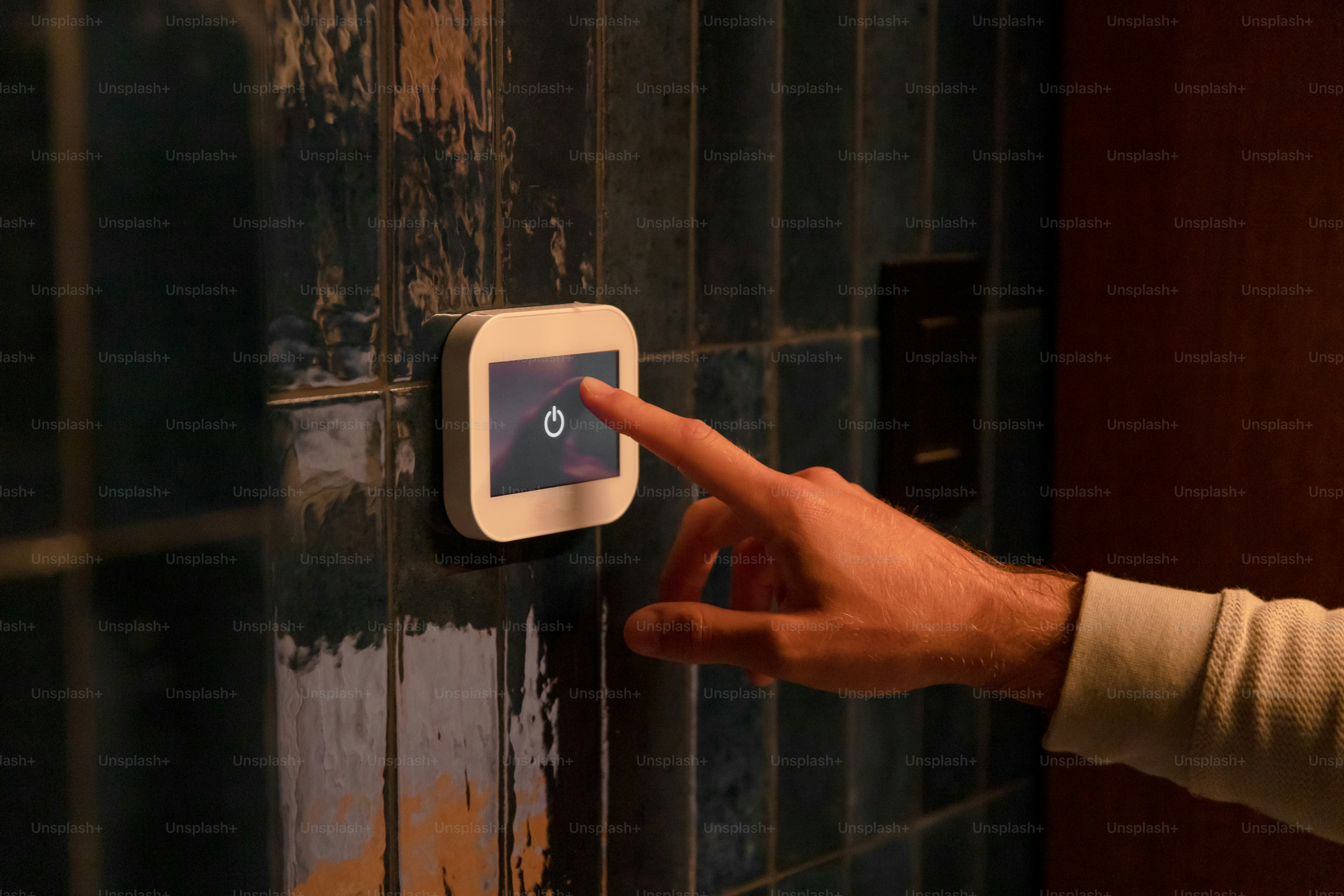 A person pressing a button on a tiled wall