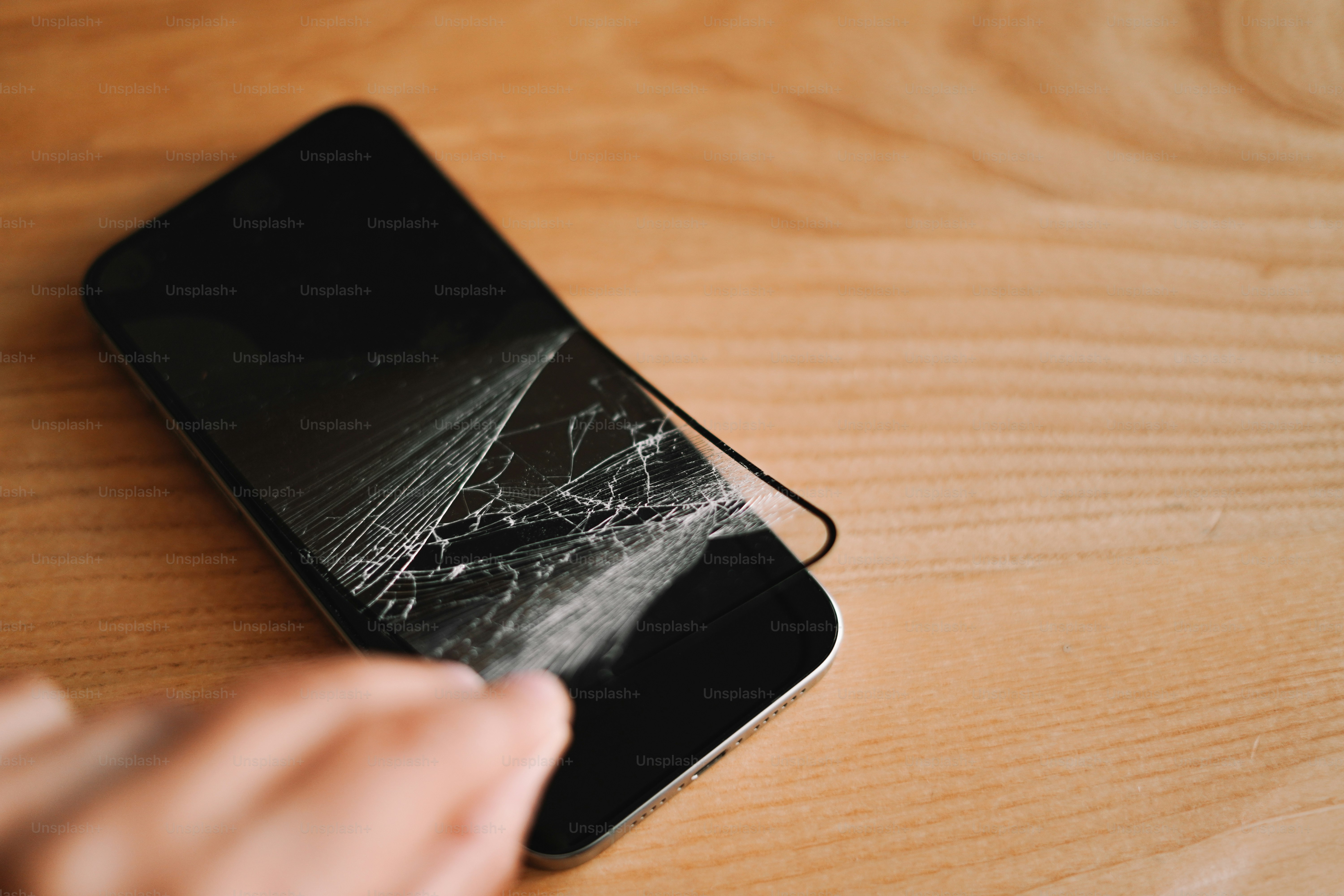 Una persona che tiene un telefono cellulare sopra un tavolo di legno