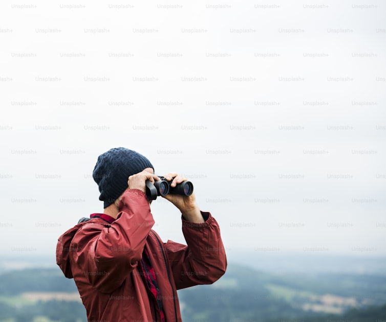 Hunter with tripod-mounted spotting scope glassing a wide western canyon at dawn